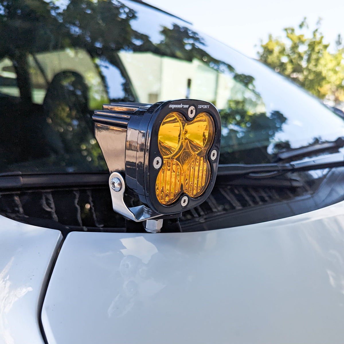 Amber LED light pod on a bracket at the base of a windshield on a white hood