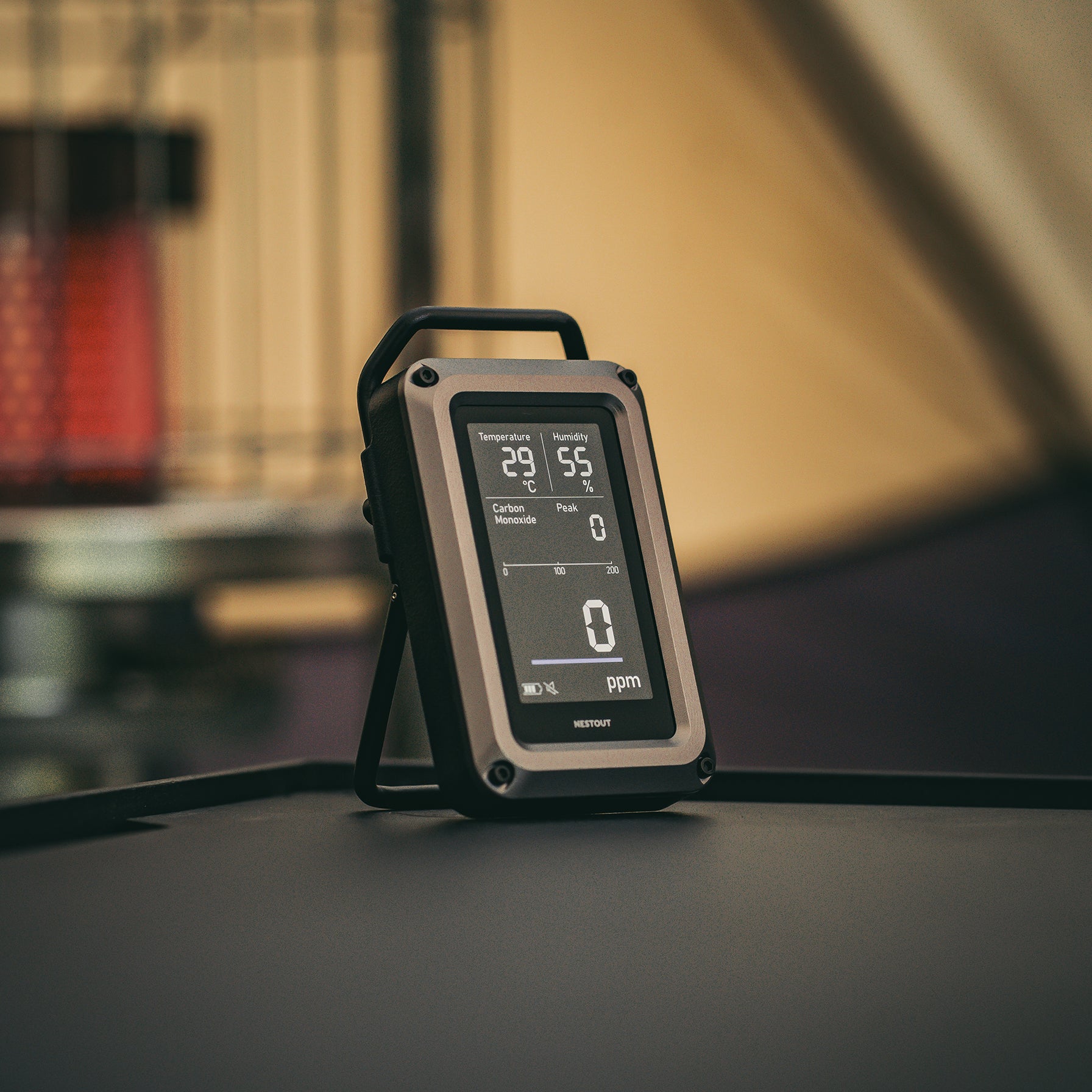 NESTOUT CO Alarm propped on its kickstand outdoors near a tent, screen showing 29°C, 55% humidity, and 0 ppm carbon monoxide
