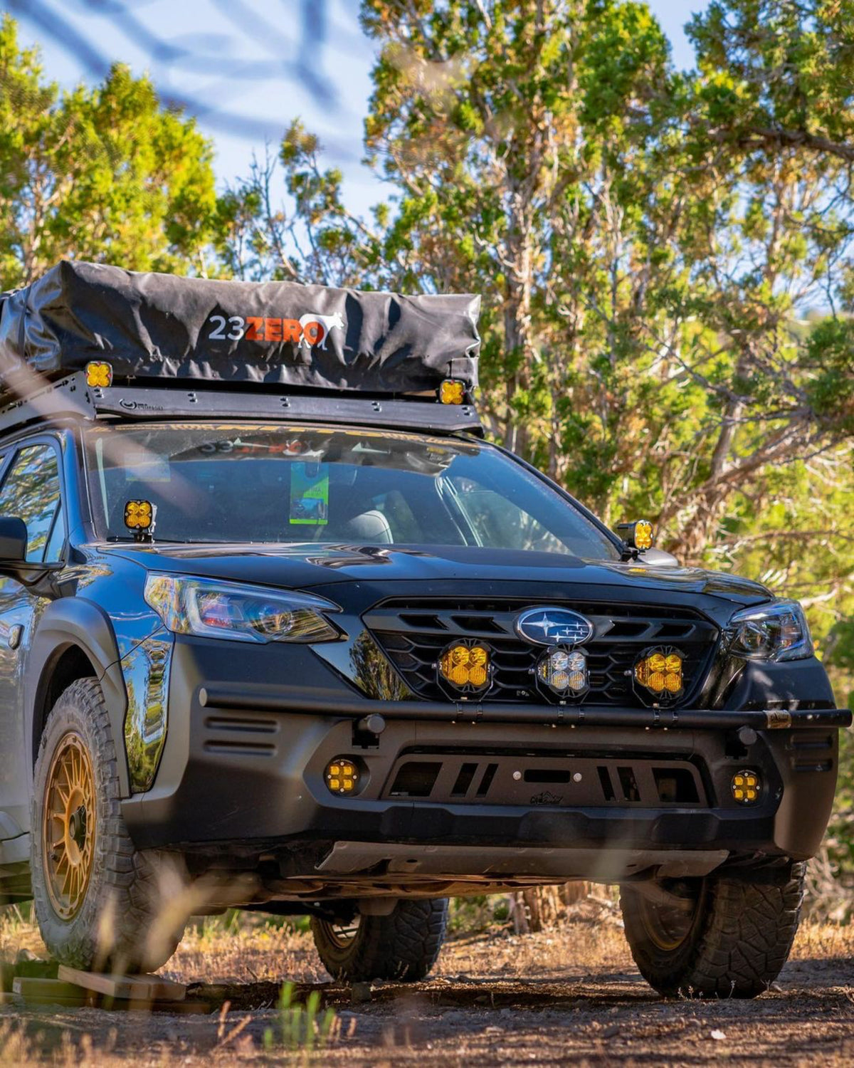 Subaru wagon with a rooftop tent and amber light pods in a wooded setting