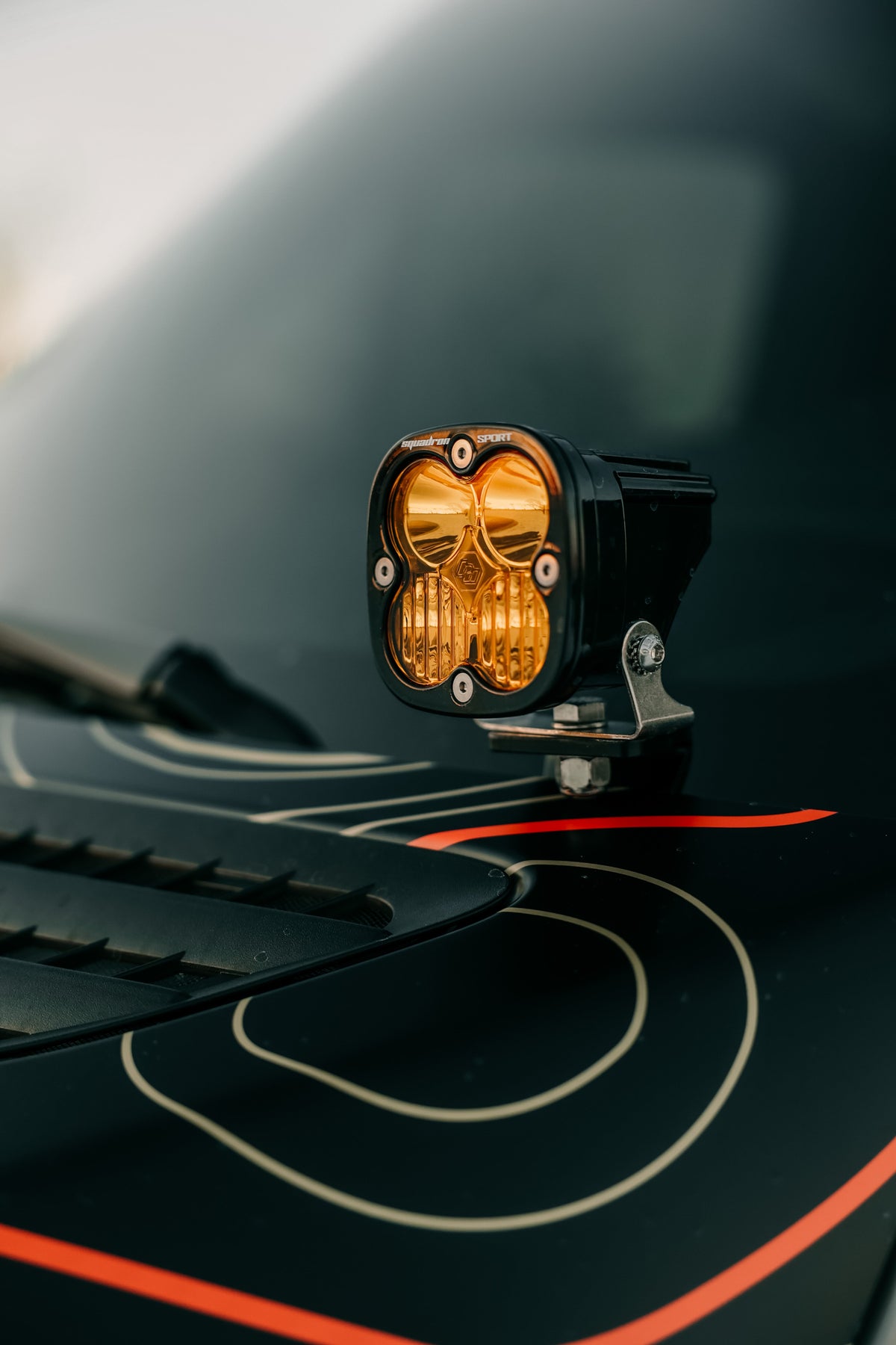 Amber LED light pod on a bracket mounted on a dark hood with orange trim
