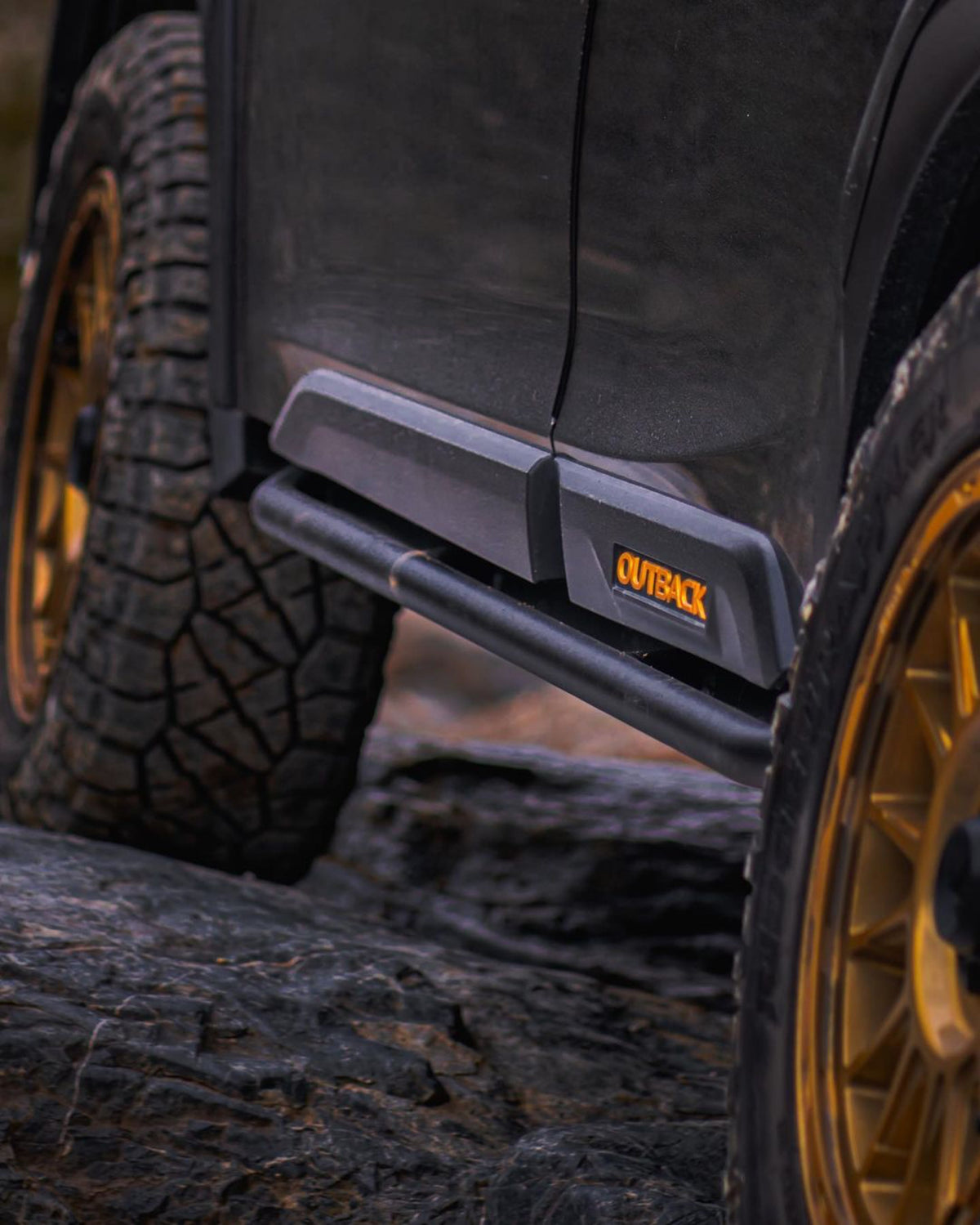 Black rock slider mounted along the lower body of a dark SUV beside a front wheel