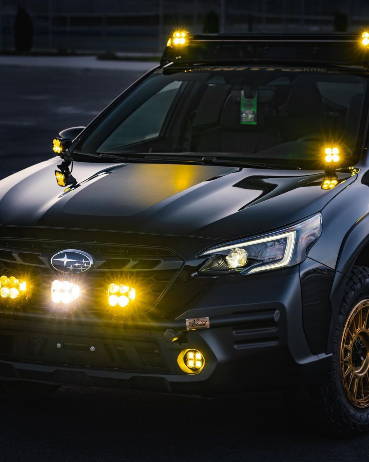 Dark Subaru wagon at night with amber light pods on the hood and bumper