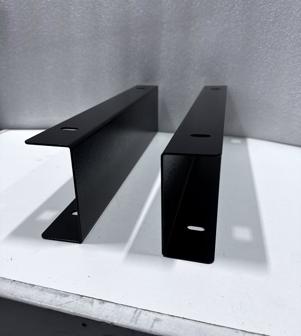 Pair of black Mid Deck riser brackets standing on a bench