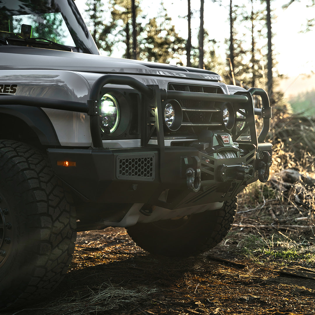 Close view of the bull bar and headlight on the front of a silver SUV in a forest