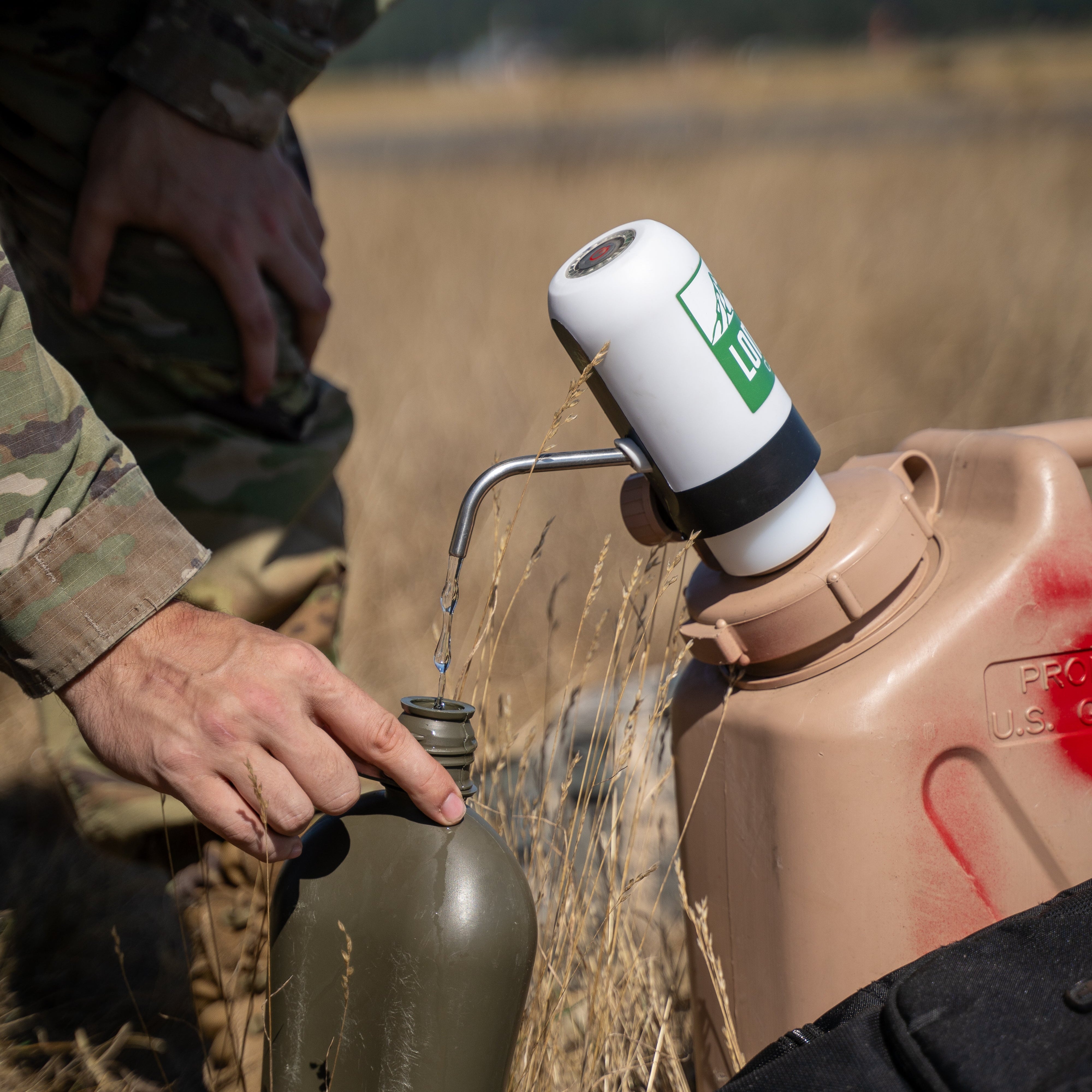 Soldier in camo filling a canteen from the Lone Rock Concepts pump on a tan military water can