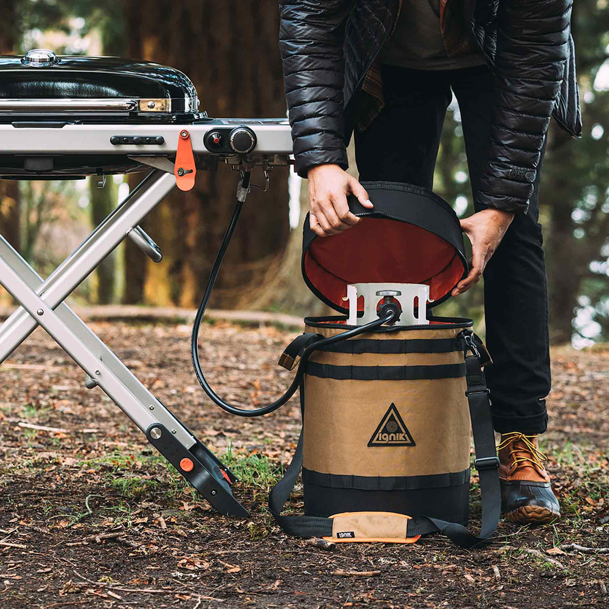 Ignik 20lb tank case seat – person lifting the lid beside a camp stove