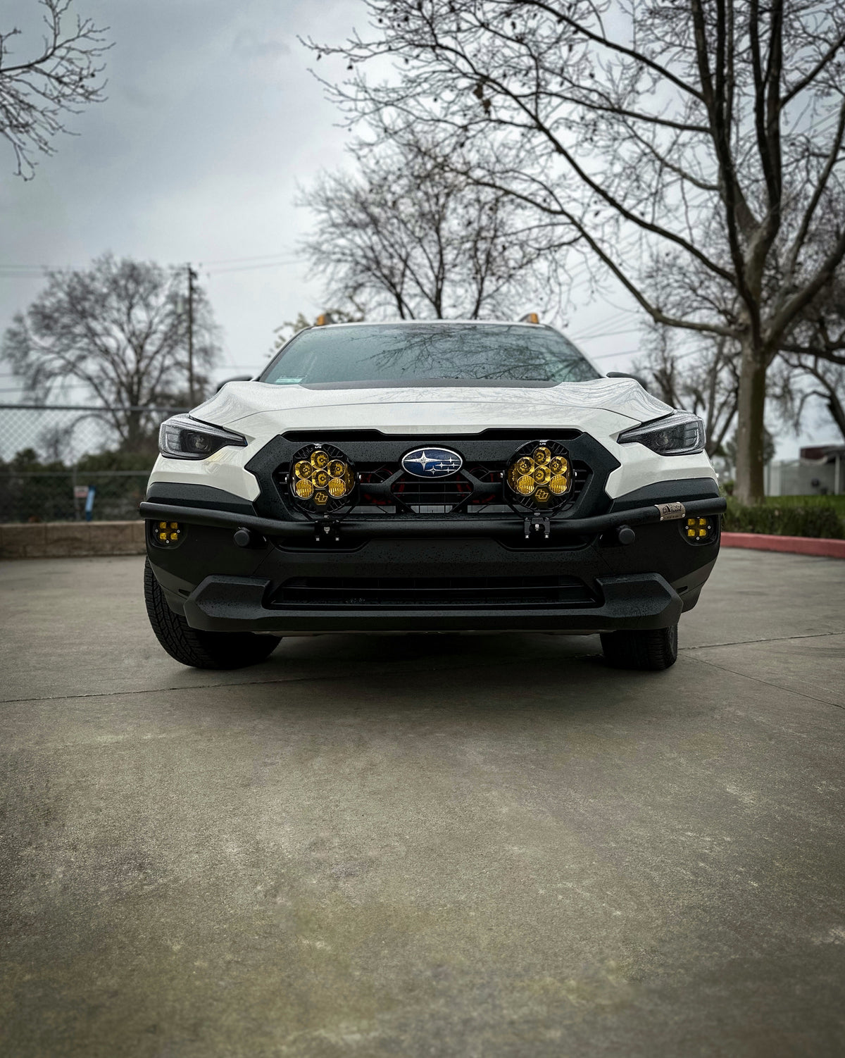 Front view of a white Subaru SUV with a brush bar and amber light pods