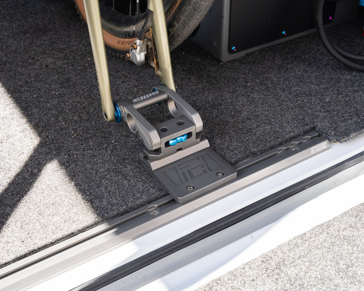 Offset plate holding a fork mount and bike on L-track beside a vehicle door sill