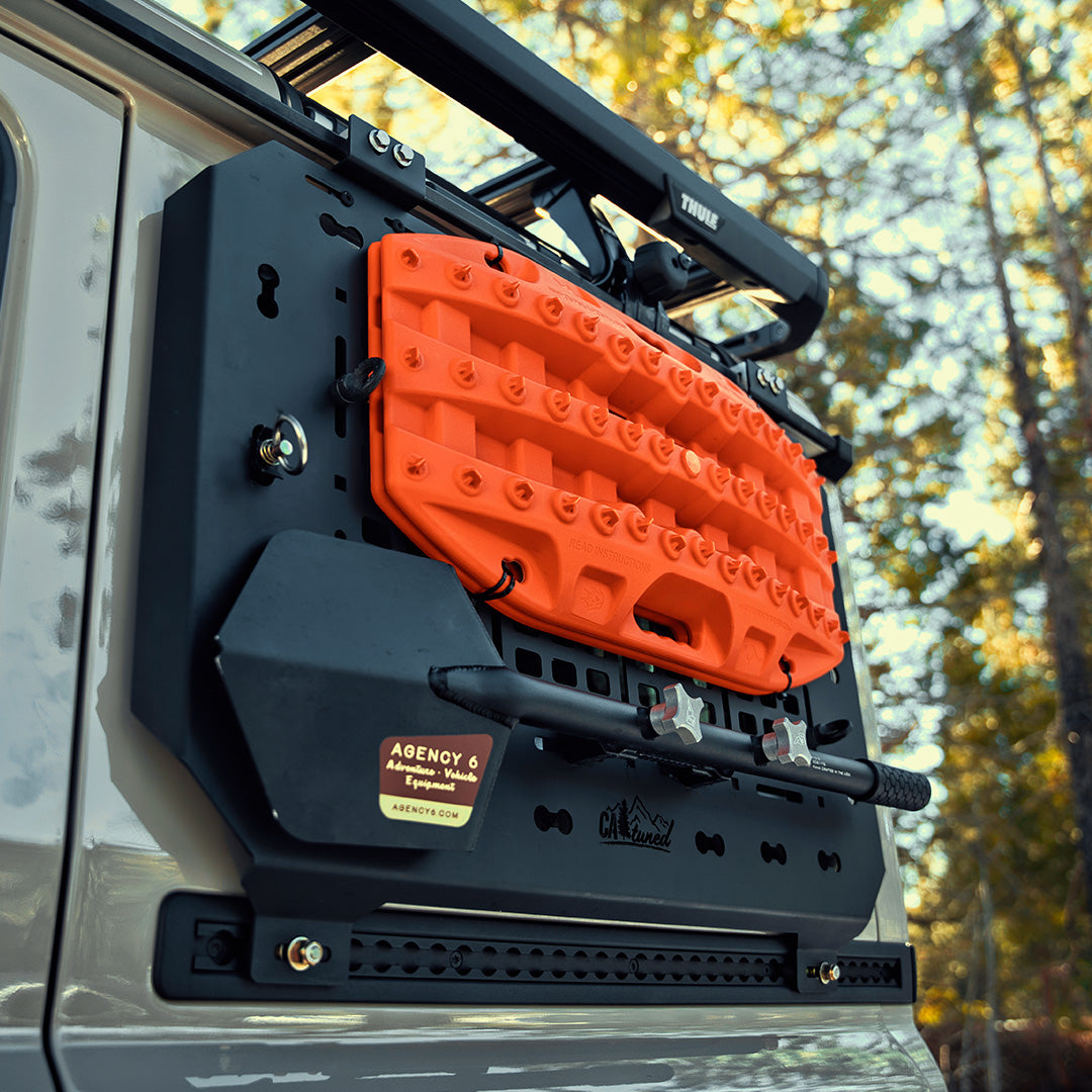 Black MOLLE panel on a vehicle door holding an orange recovery board and a strap