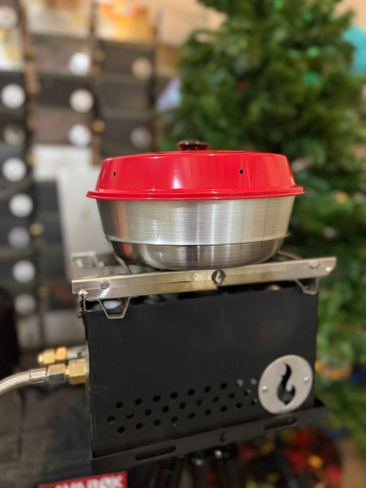 Stainless firebox topped with a mixing bowl and red lid, set up indoors near string lights in a retail display setting