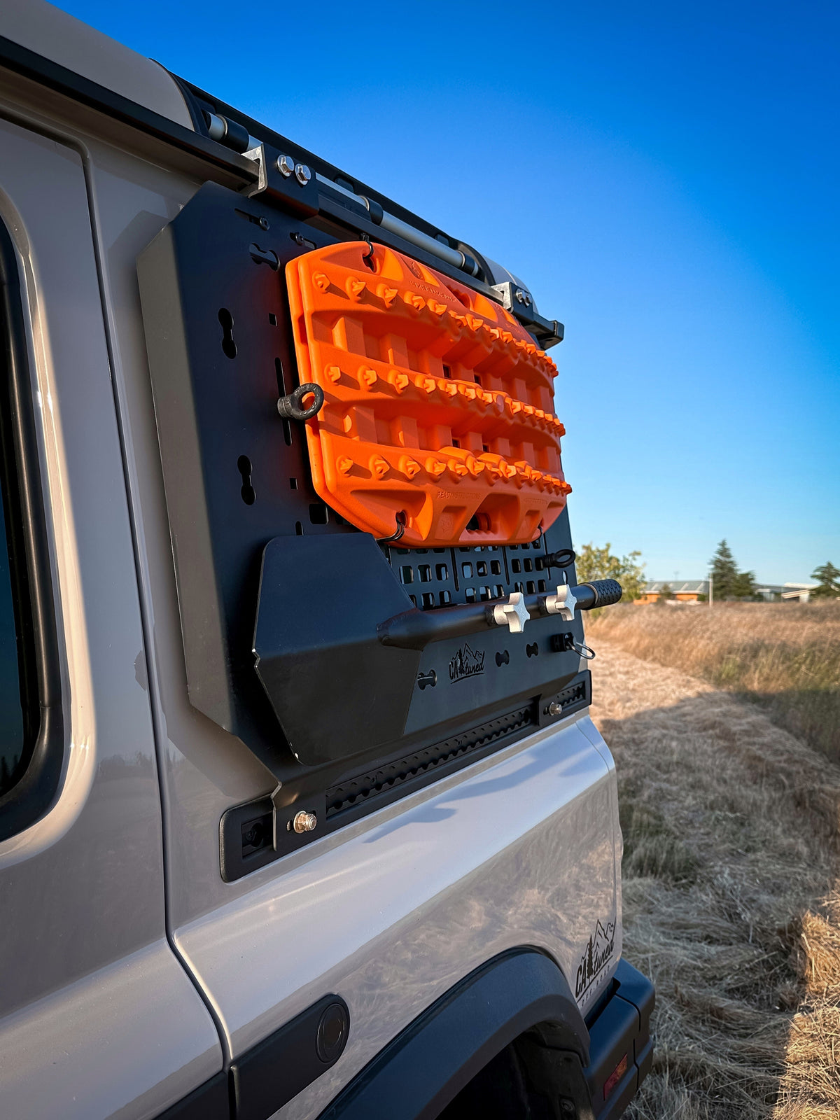 Orange recovery board mounted on the MOLLE panel on the side of a silver SUV