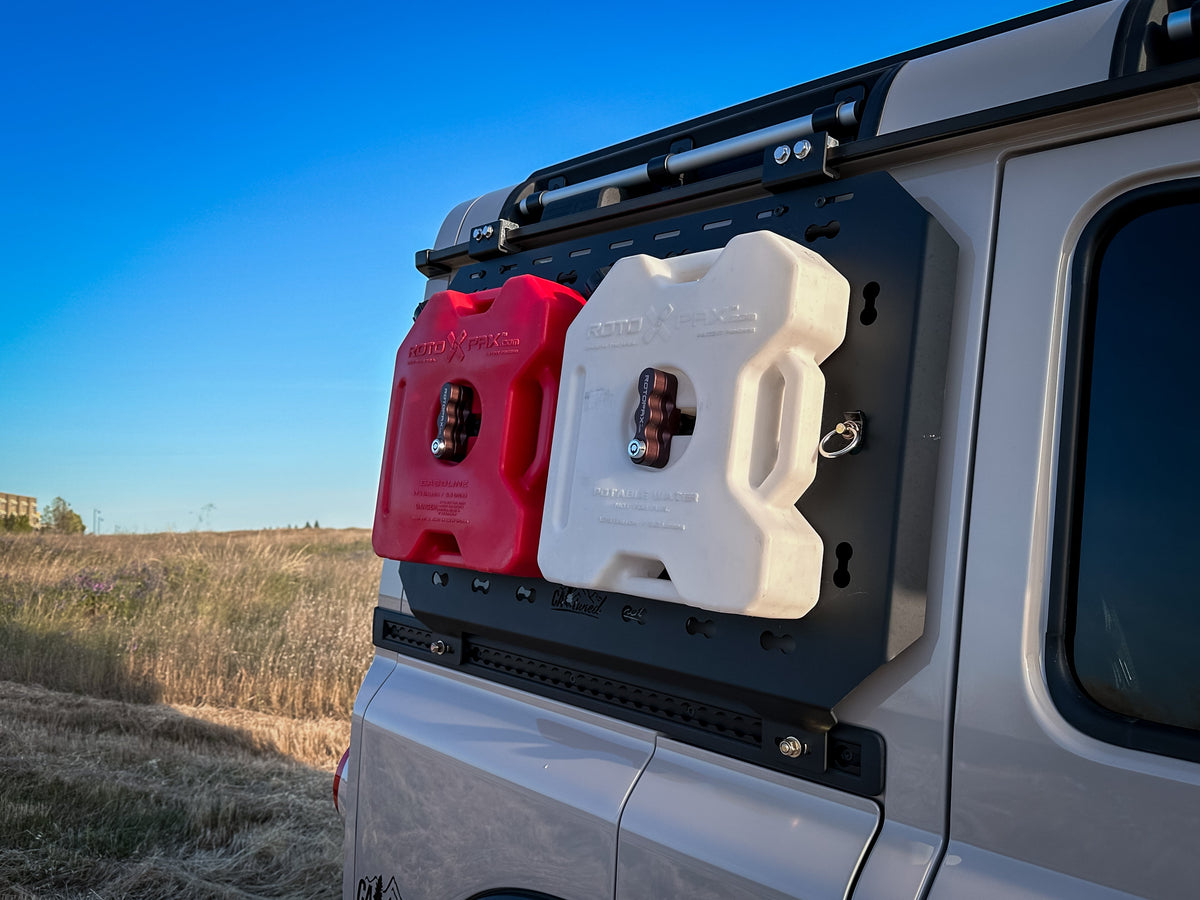 Red and white fuel cans mounted on the MOLLE panel on the side of a silver SUV at sunset