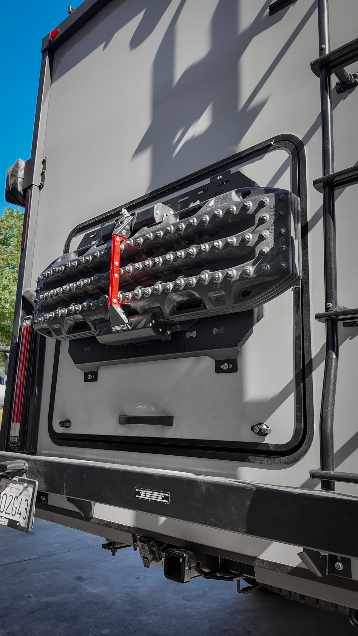 Recovery boards with a red strap on a MOLLE panel on a van door