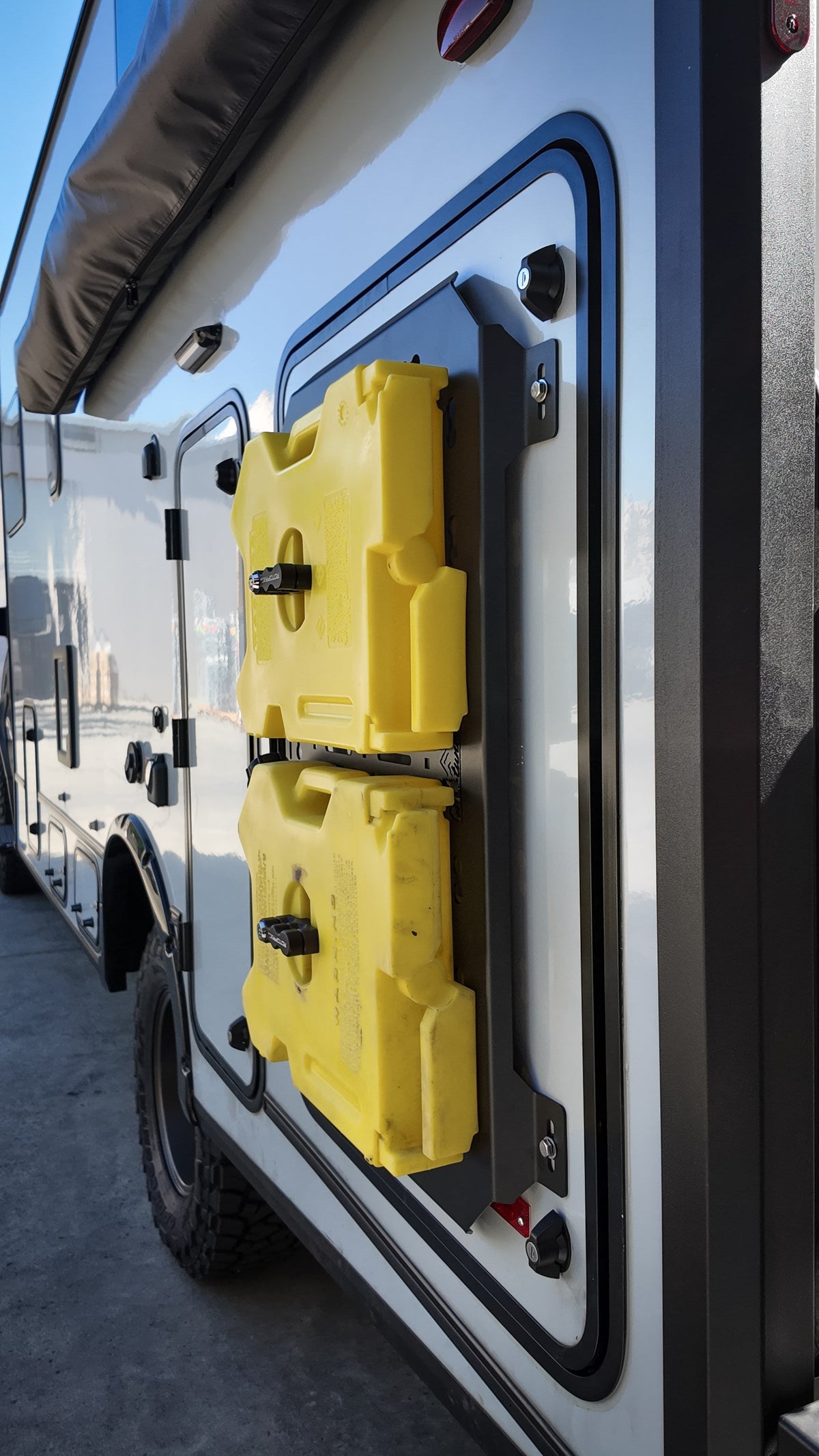 Two yellow fuel cans mounted on a MOLLE panel on the side of a van