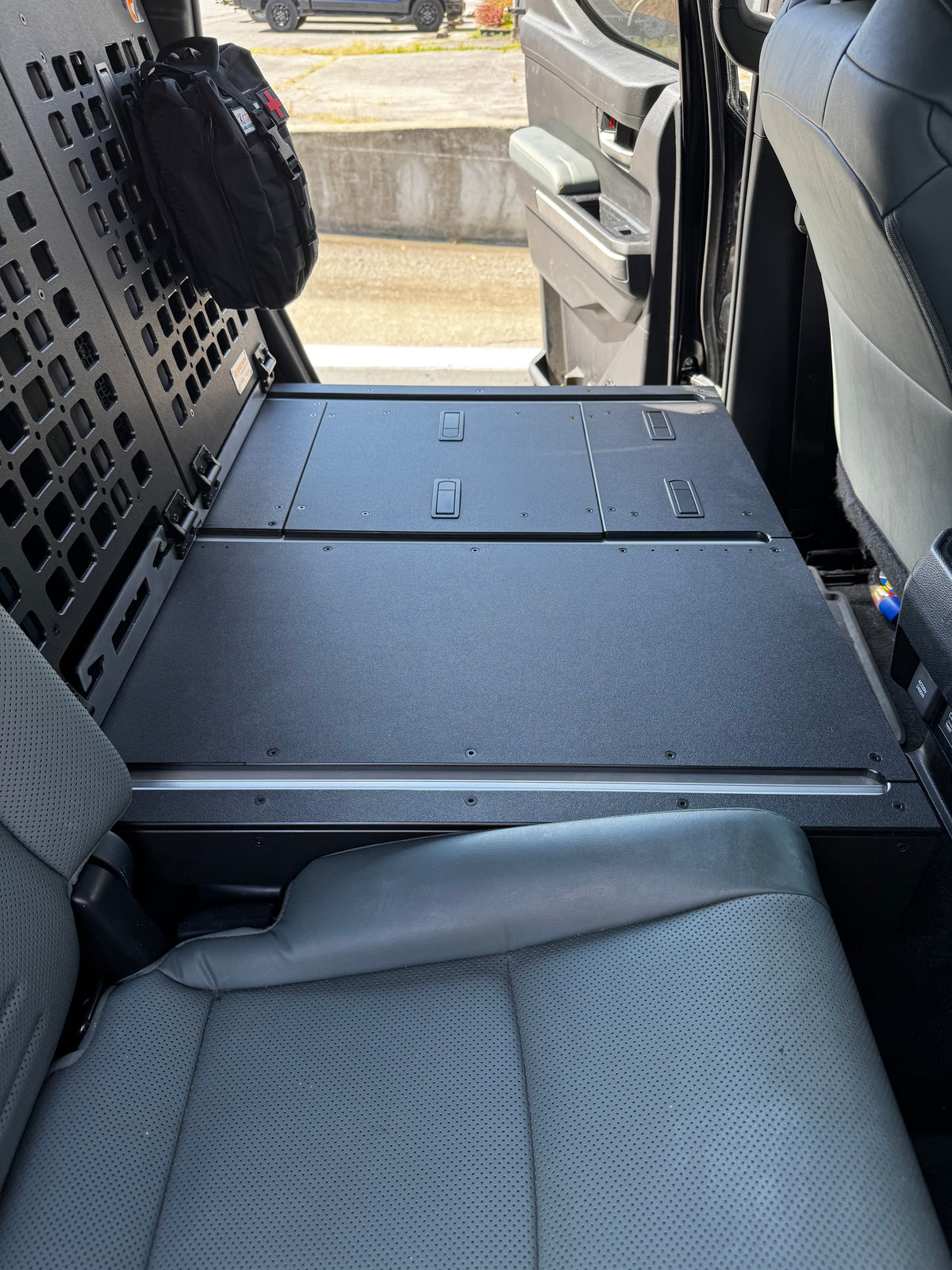 Top view of the CargoKits seat delete platform showing four recessed latch hatches and a silver accessory rail along the front edge, with the MOLLE panel at left