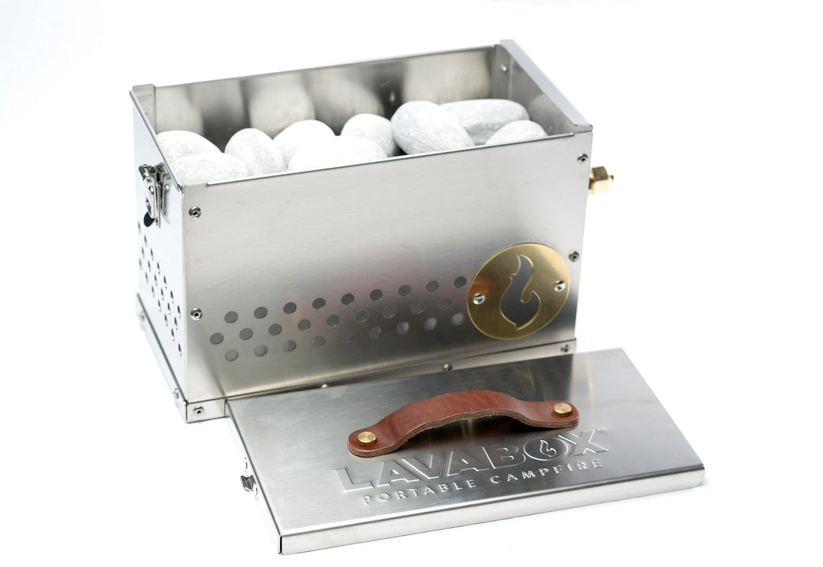 Stainless Hekla LavaBox firebox open and filled with light gray Hades Stones, with its leather-handled branded lid propped in front