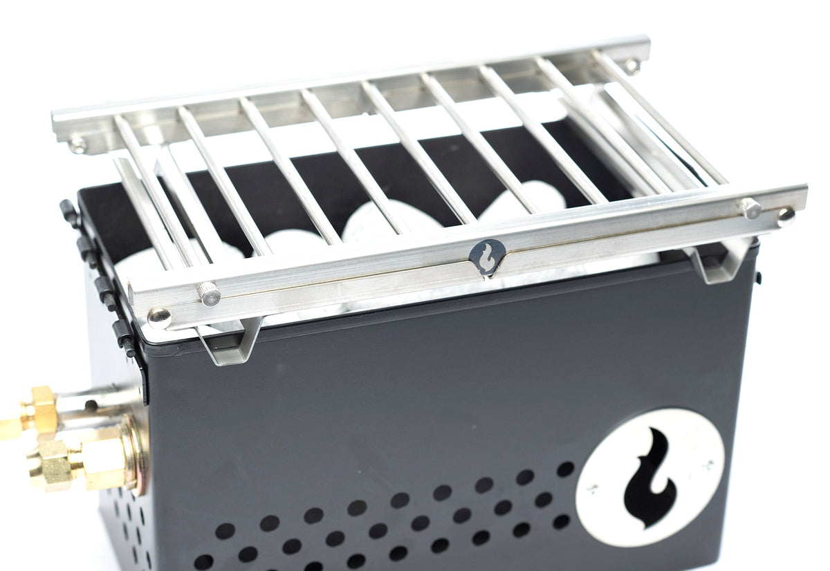 Stainless steel firebox with slotted grill grate on top, angled studio shot showing the flame logo medallion on the side panel