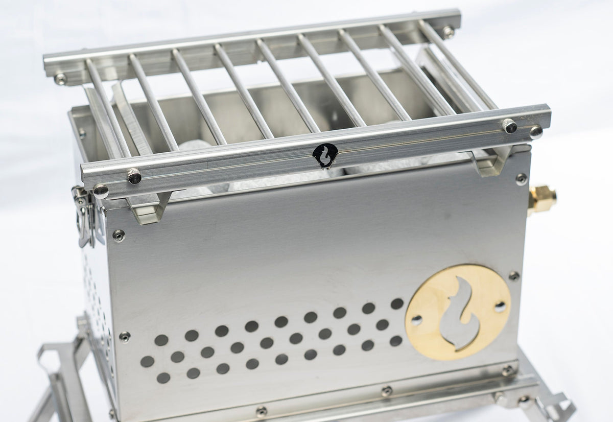 Stainless steel LavaBox firebox with a slotted grill grate on top and perforated air vents on the side, studio shot