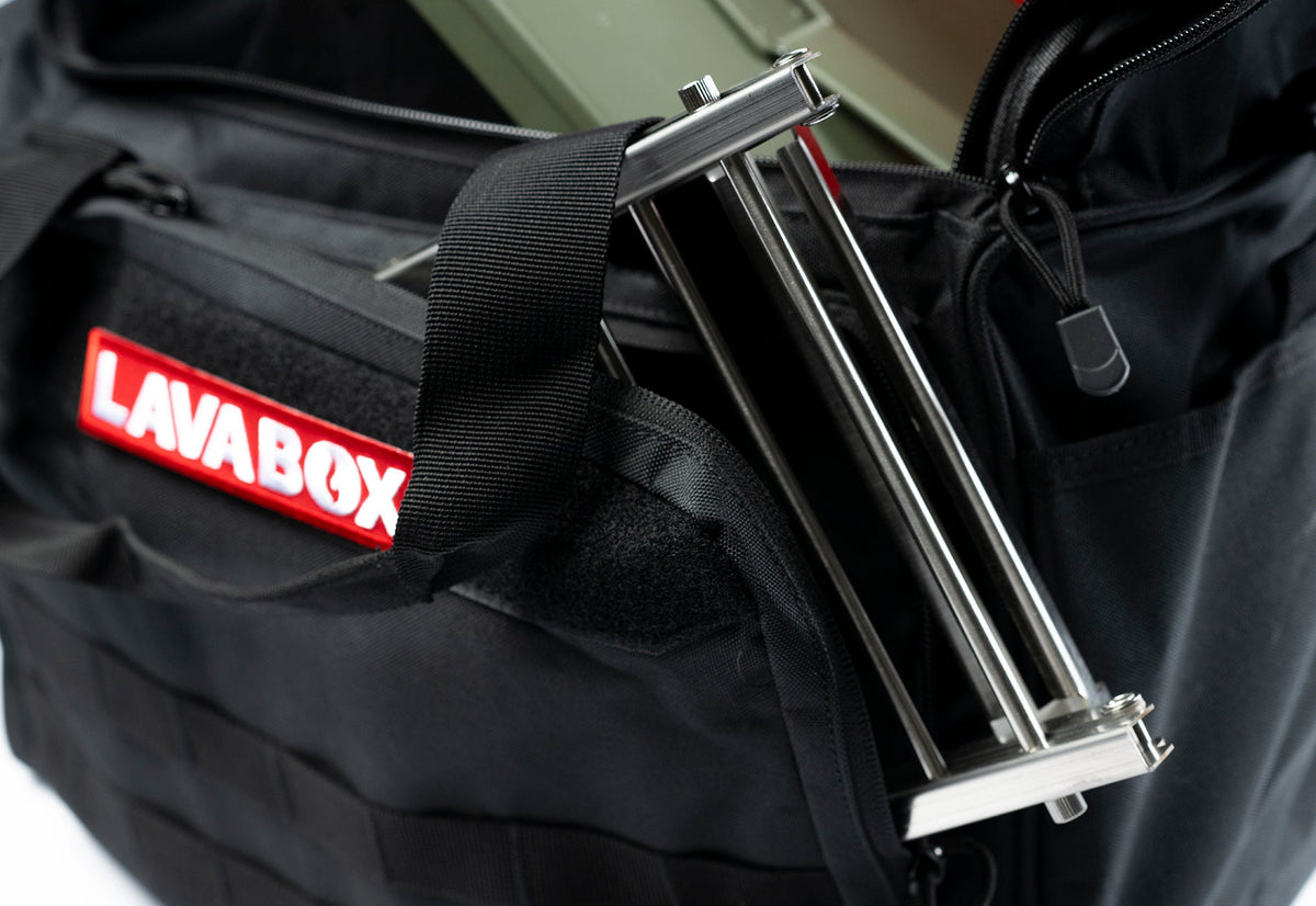 Close-up of a folded stainless steel accessory stand leg strapped to the side of a black LAVABOX carry bag