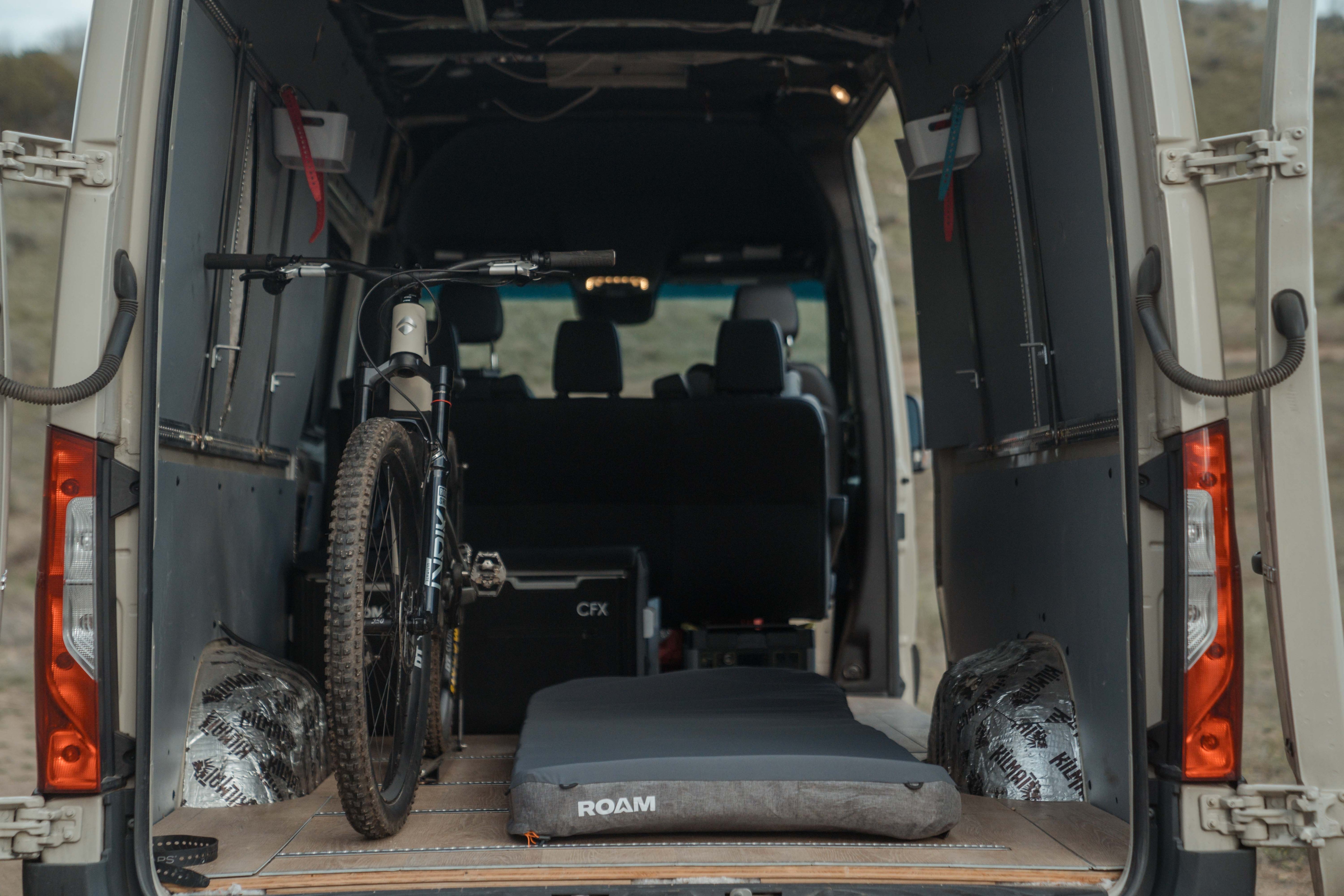Van interior with a bicycle and camping gear, parked outdoors.