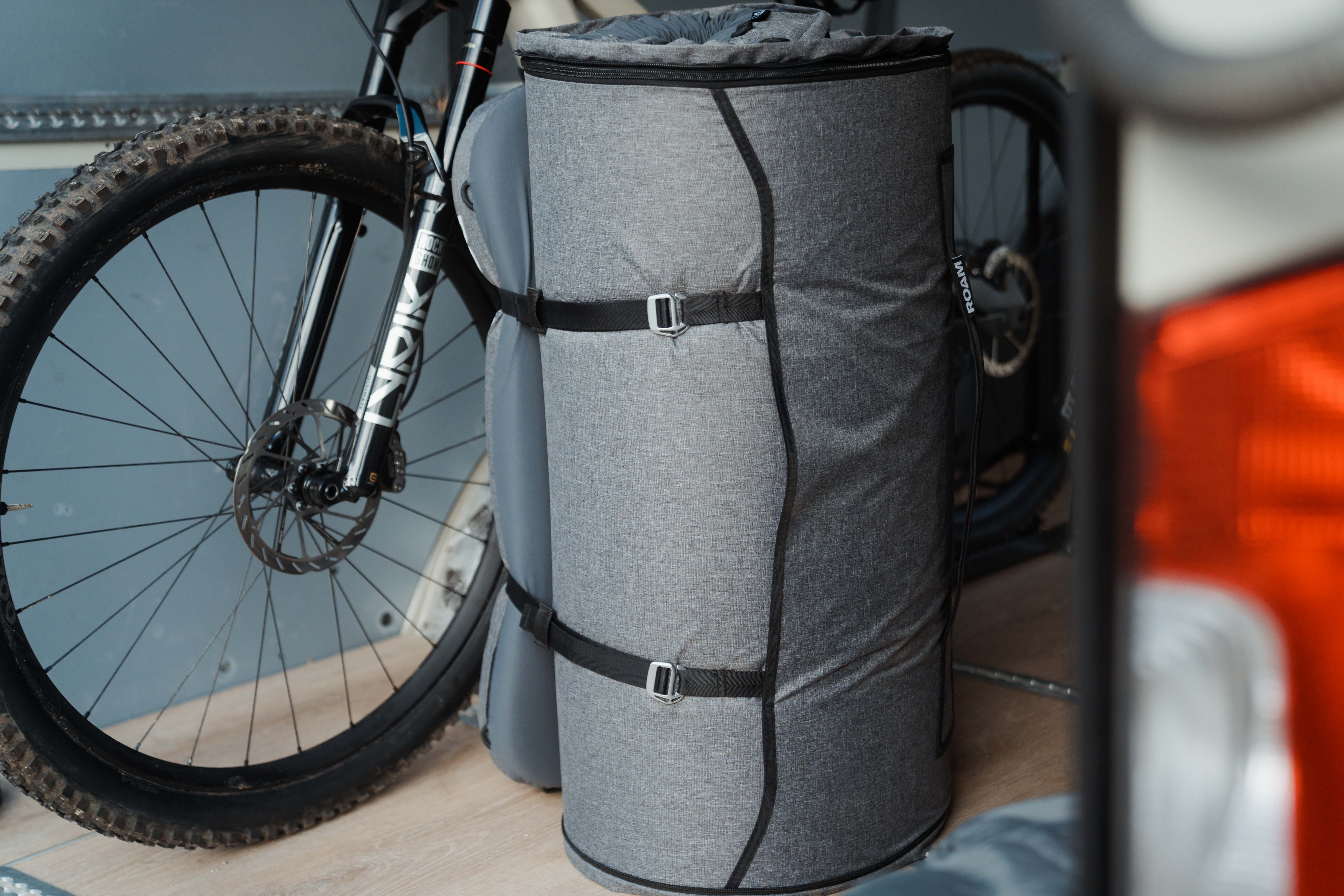 Gray mattress with straps attached to a bicycle on a wooden floor.