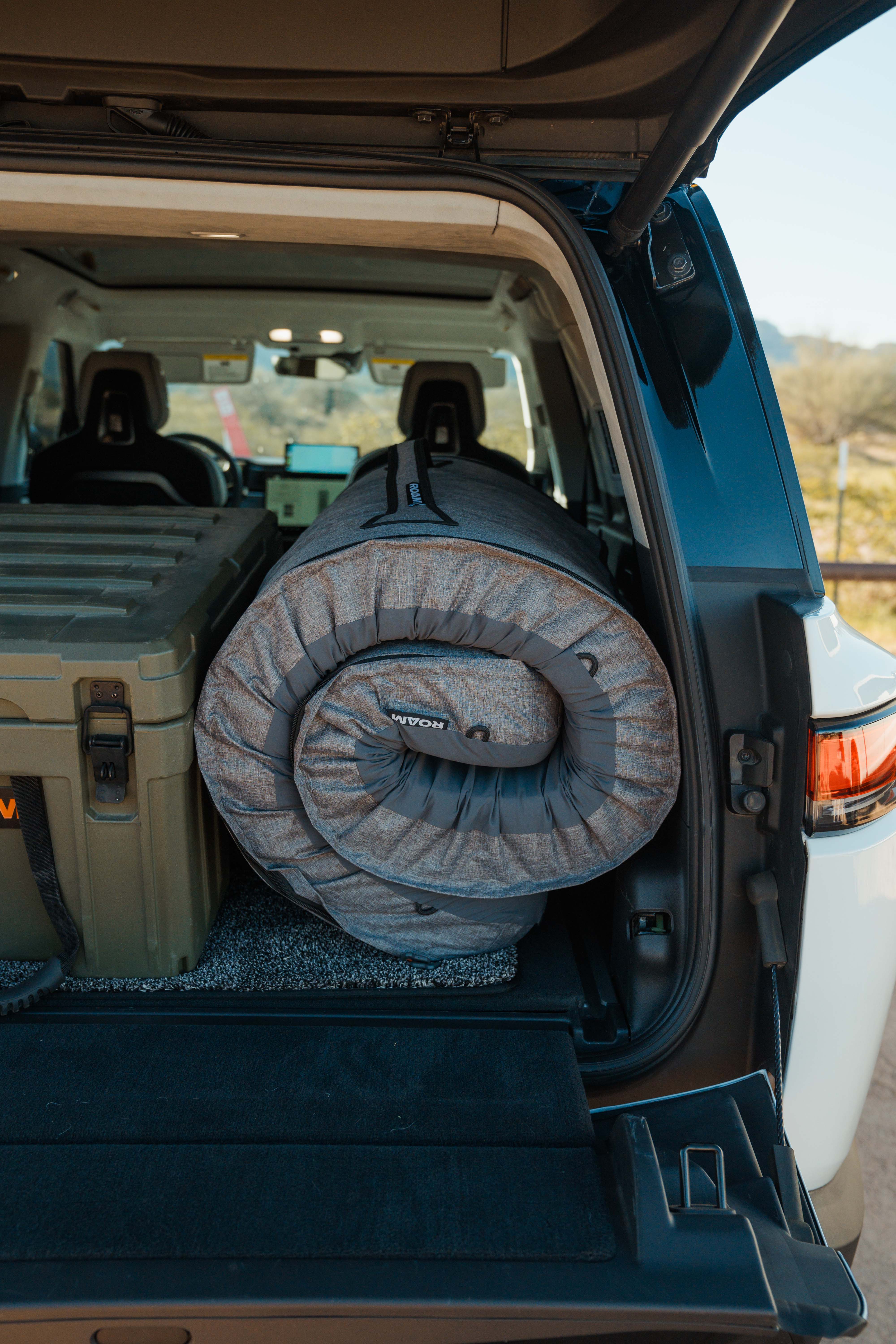 Open car trunk with rolled roam mattress and storage box in a desert setting
