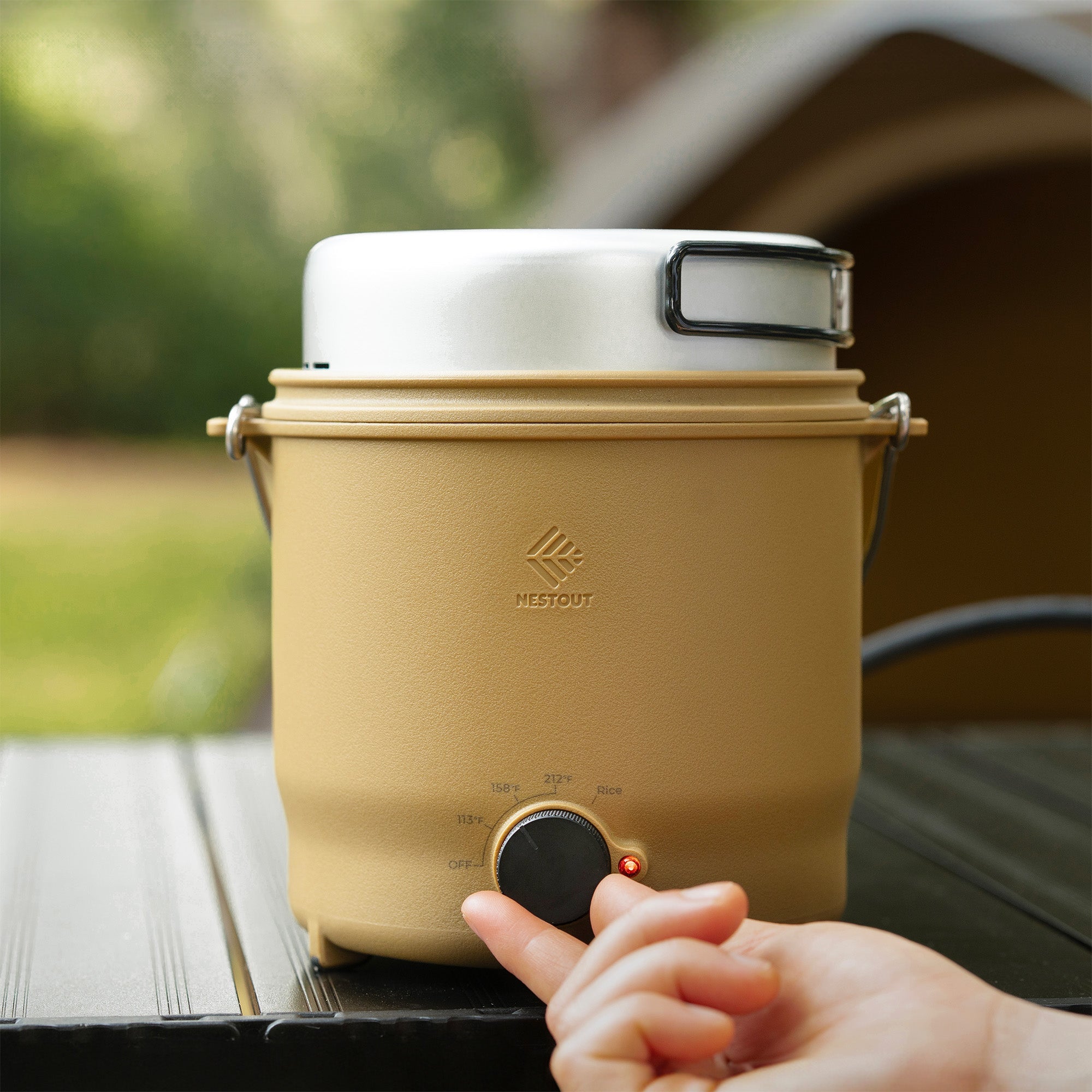 Front view of the NESTOUT cooker's control dial (113°F/158°F/212°F/Rice) with a finger near the lit red power indicator