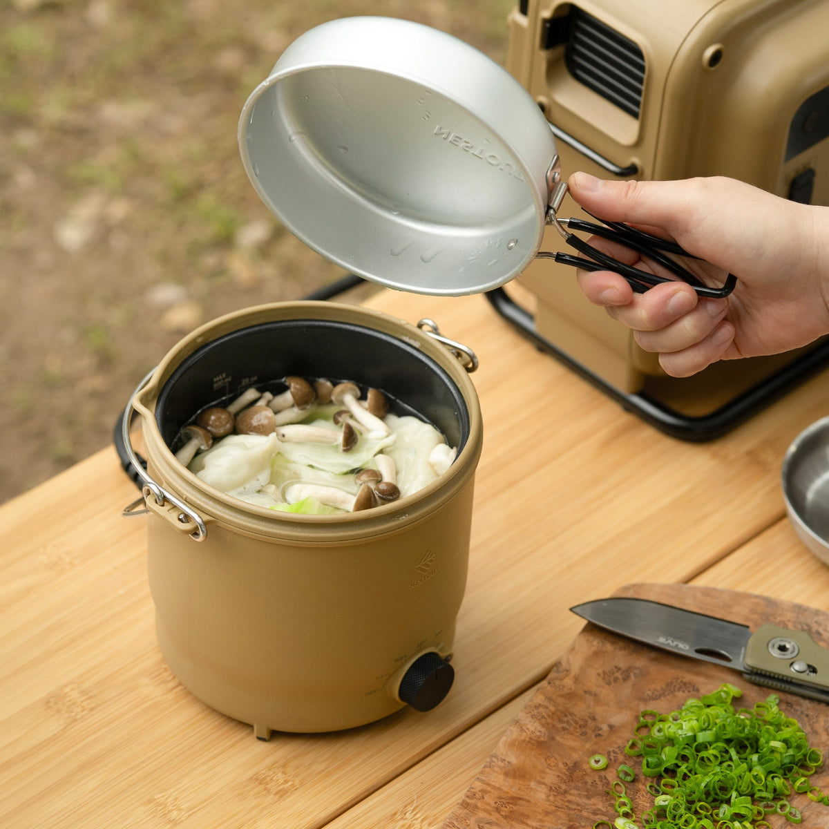 Lid lifted off the NESTOUT cooker revealing mushrooms and dumplings simmering in broth inside