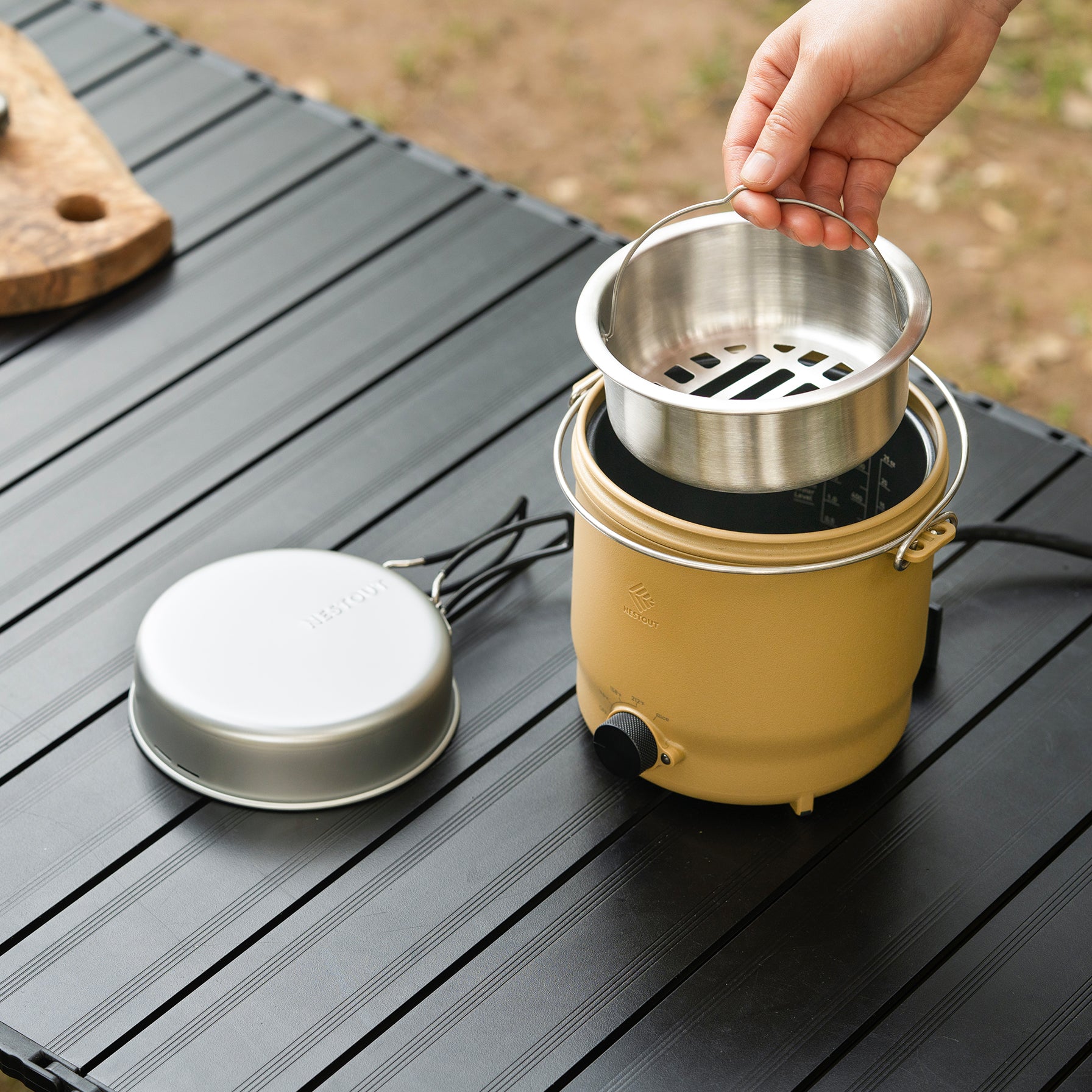 Lowering the steaming tray insert into the NESTOUT cooker's pot with the lid set aside
