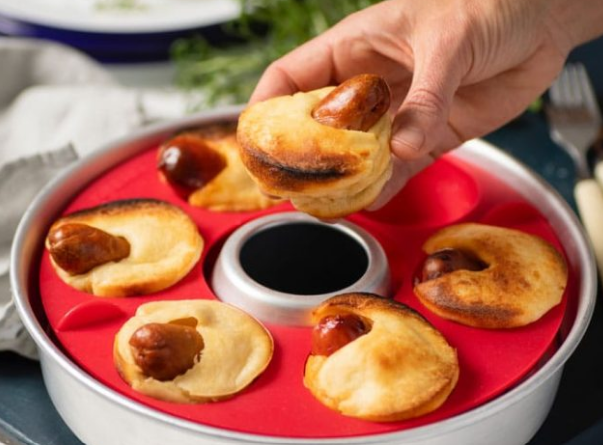 Hand holding a pastry with a hot dog inside, placed on a Omnia silicone red tray.
