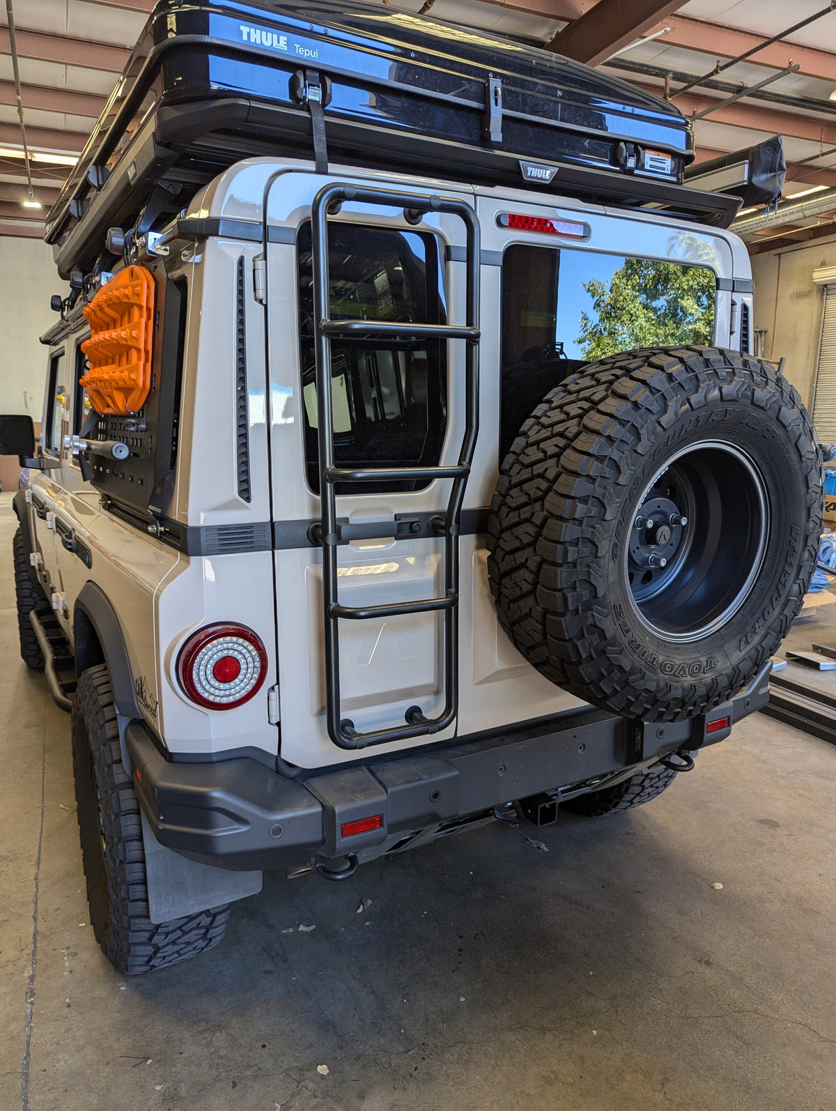 Rear of a white SUV with a spare tire, ladder and roof rack