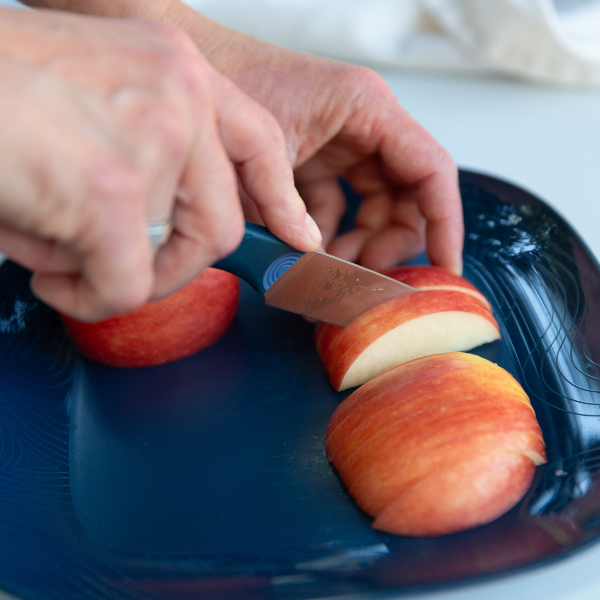 Close-up of a hand slicing an apple with the UCO Camp Paring Knife on a blue plate