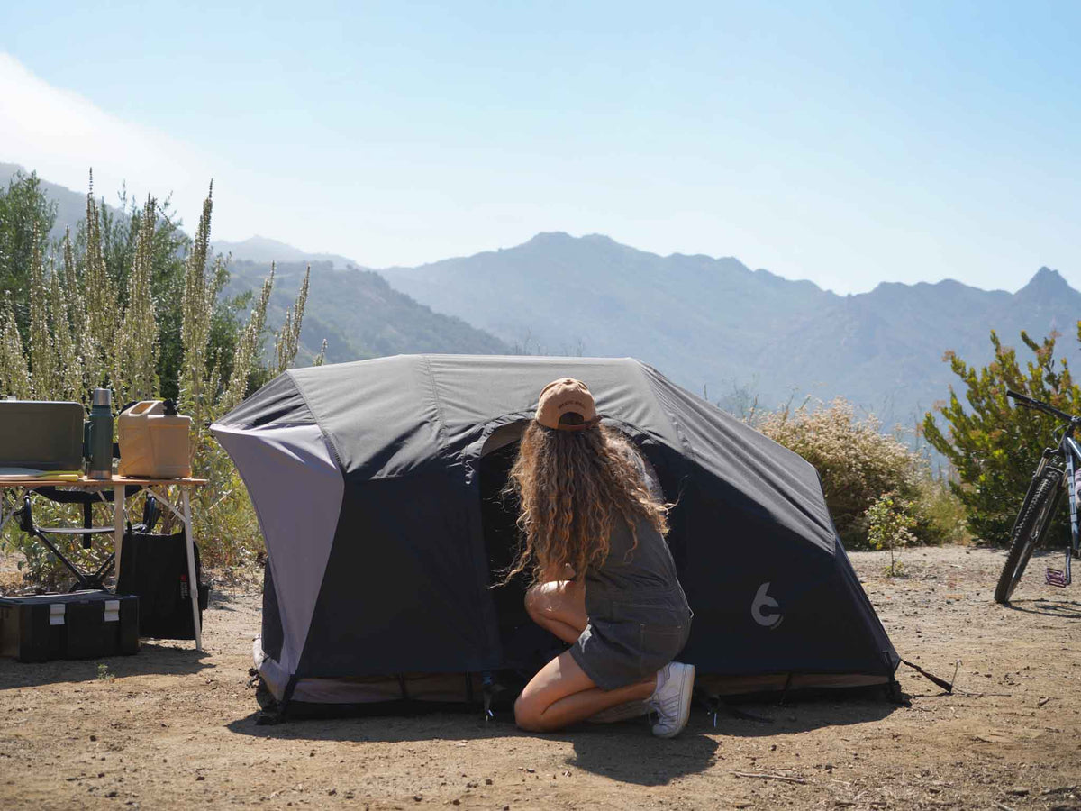 C6 Rev Rooftop Tent X (Eclipse) – person setting up a dark ground tent at camp