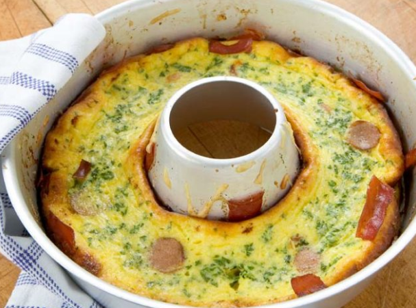 Close-up of a baked bundt-style dish with herbs and diced sausage, cooling near the Omnia oven's baking ring