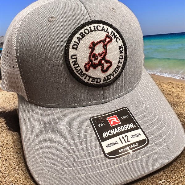 Gray-front Diabolical Inc trucker hat with white mesh by the ocean