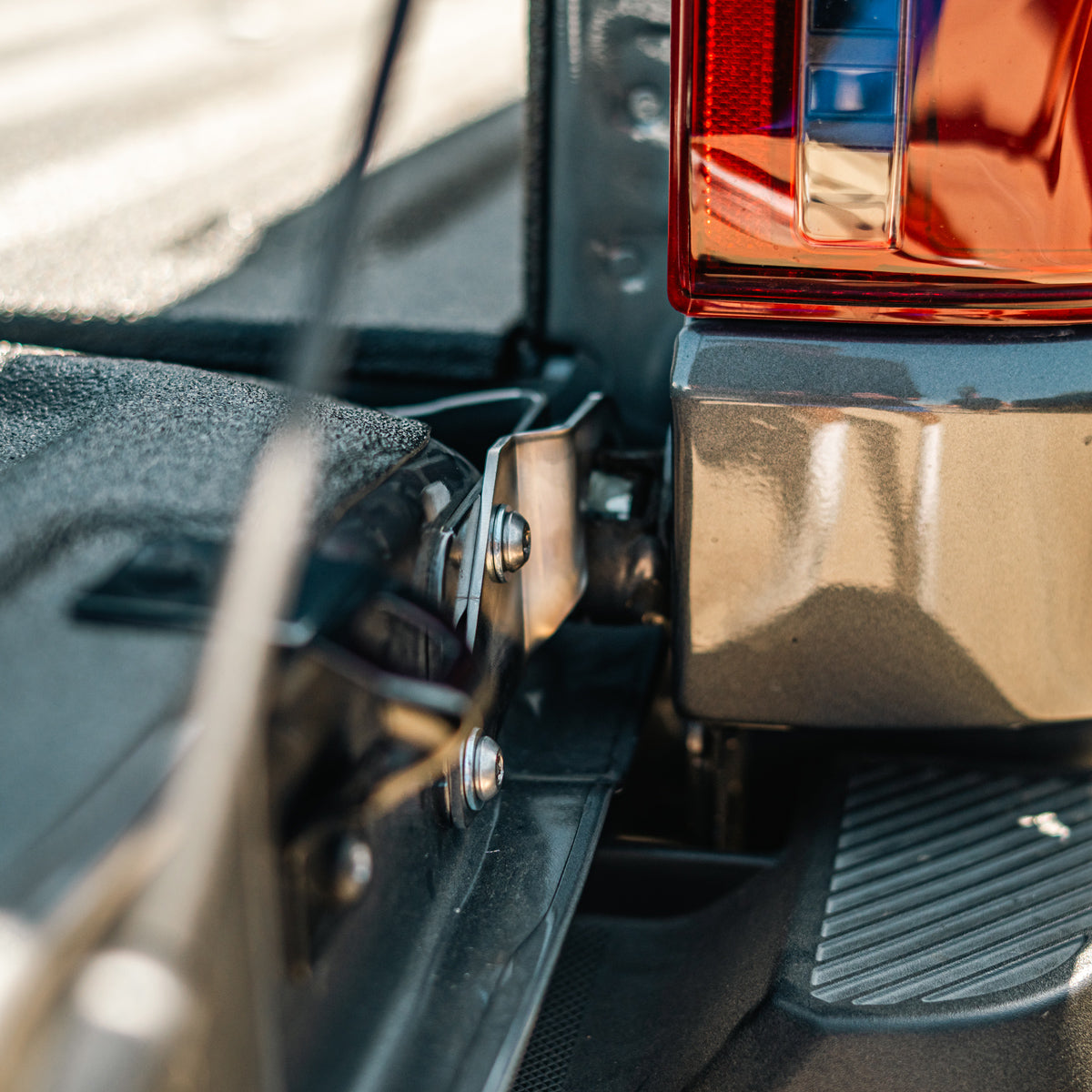Cali Raised LED tailgate theft protector installed on a Ford F-150 tailgate hinge, close-up showing the taillight