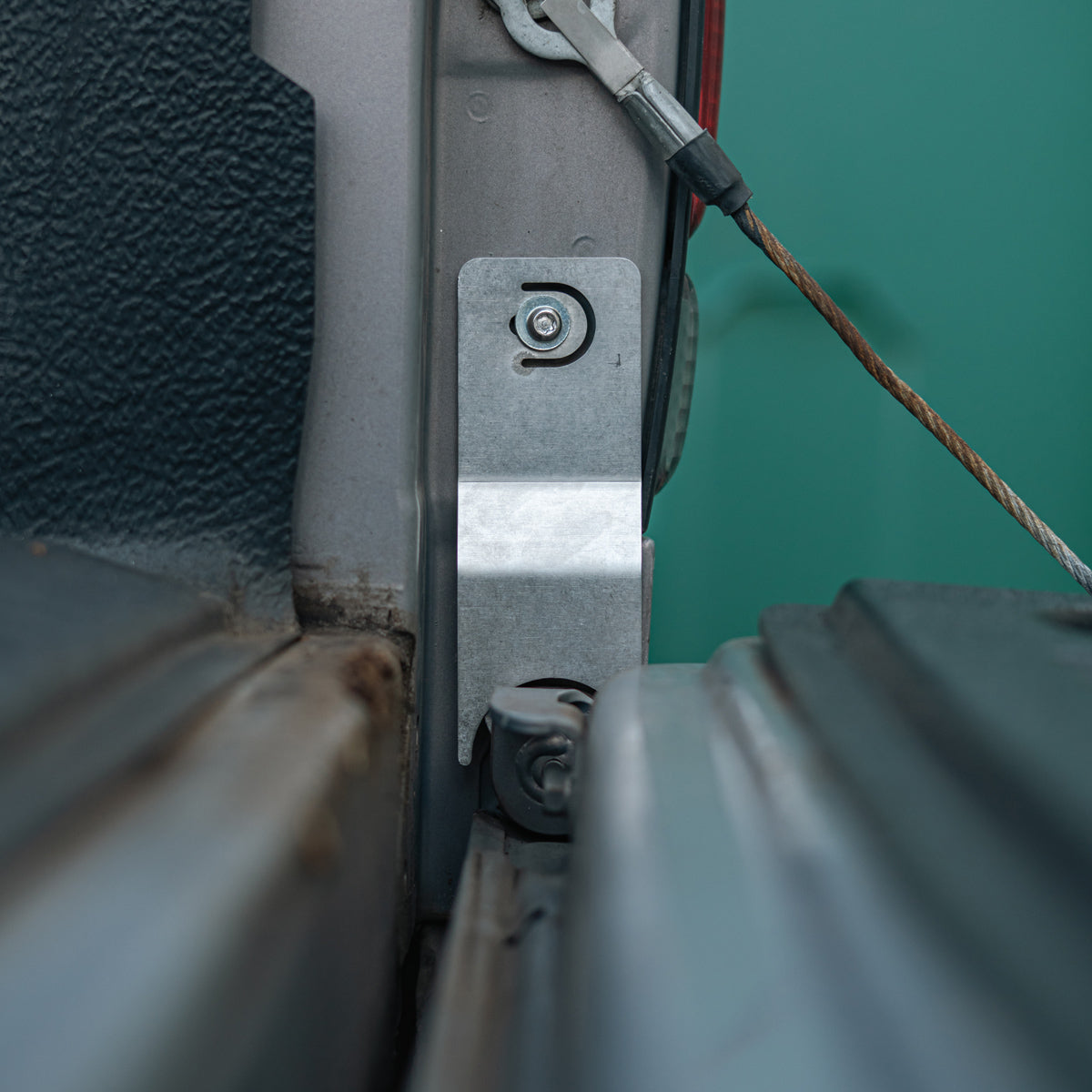 Tailgate theft protector bracket installed on the tailgate hinge area of a gray truck