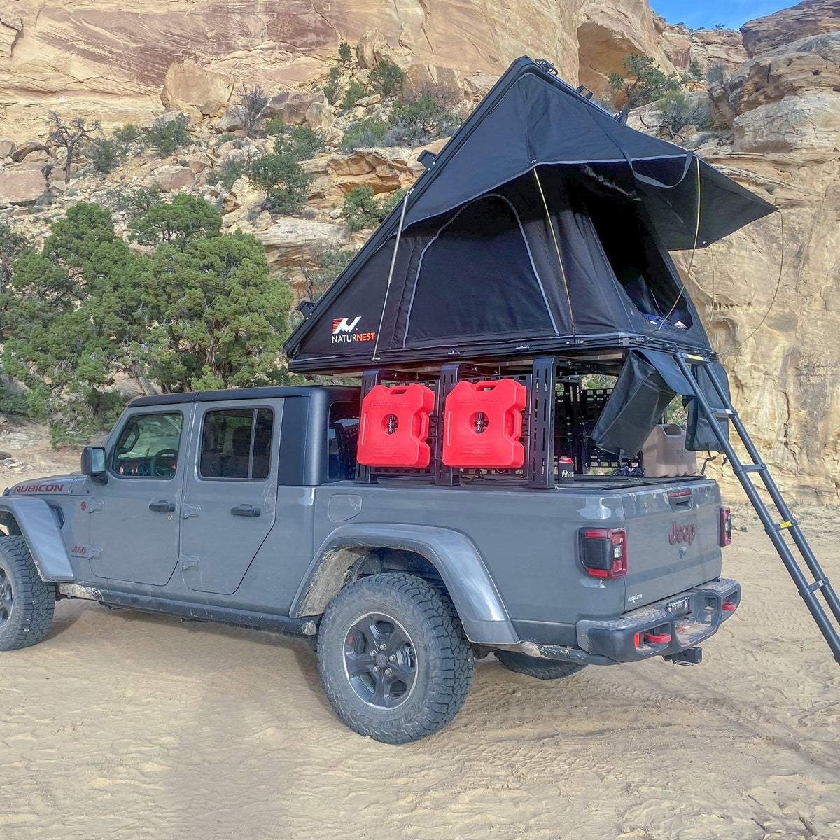 Gladiator with ROCK-IT rack, open tent and red fuel cans among desert rocks