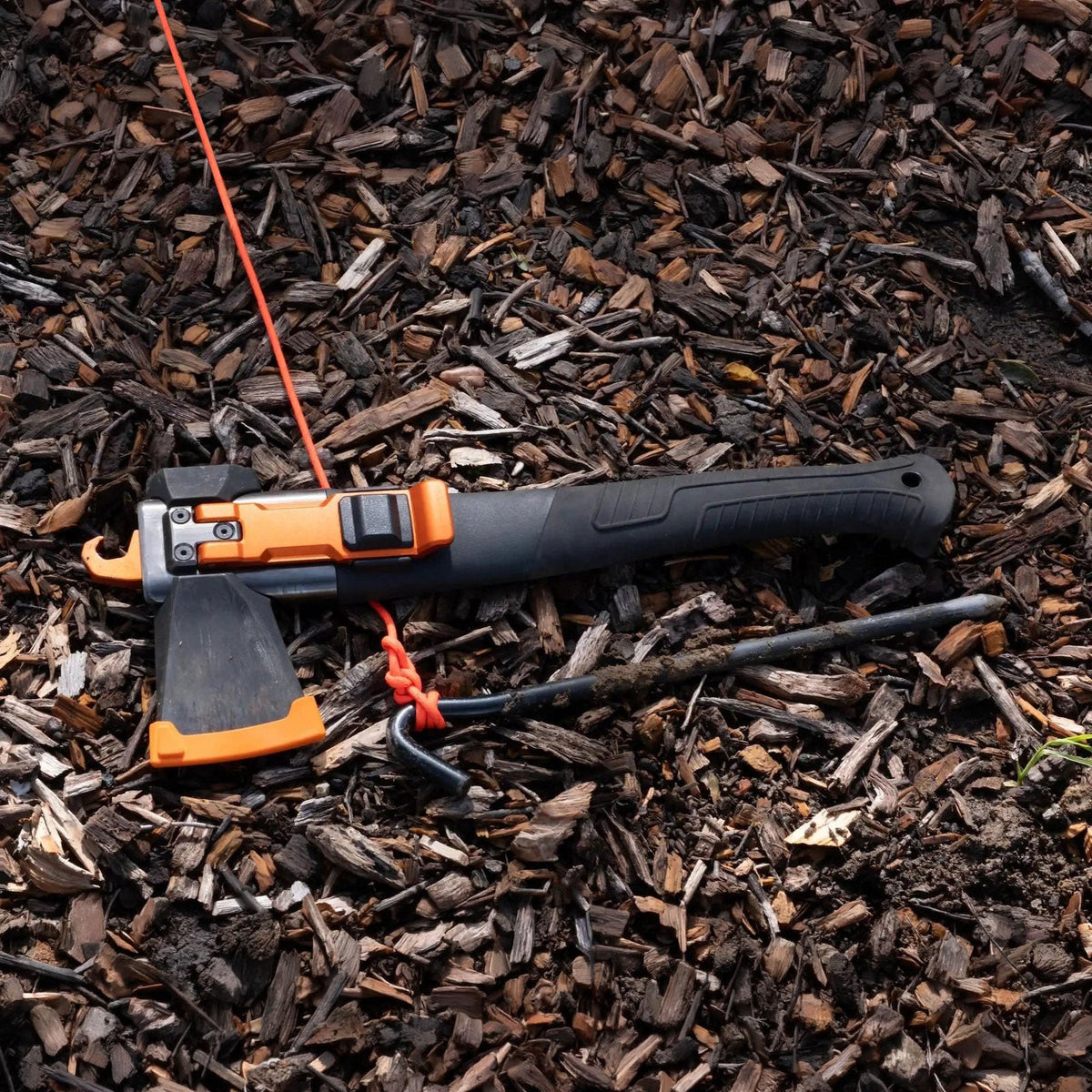 Adventure Mate axe configuration lying on wood chips with its orange hook around a tent stake and orange cord