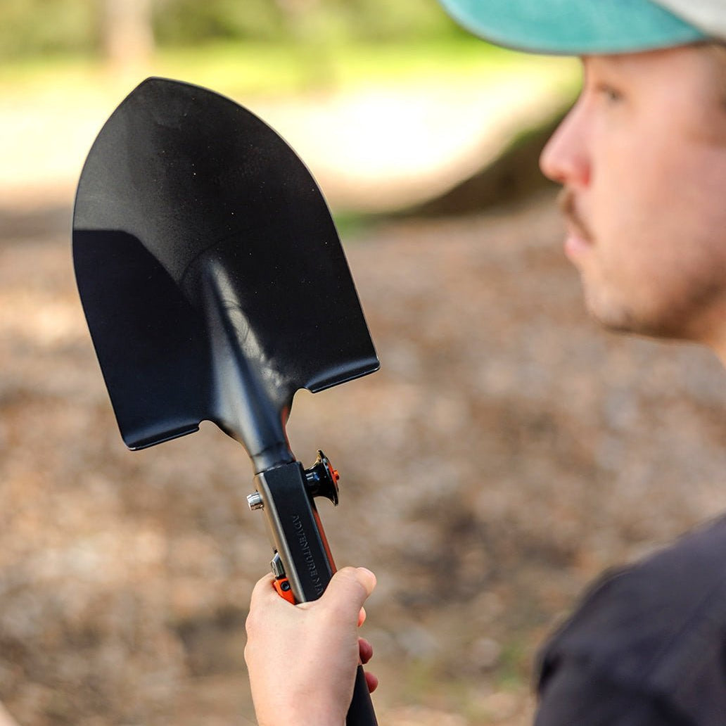 Person holding the Adventure Mate shovel upright by its handle outdoors