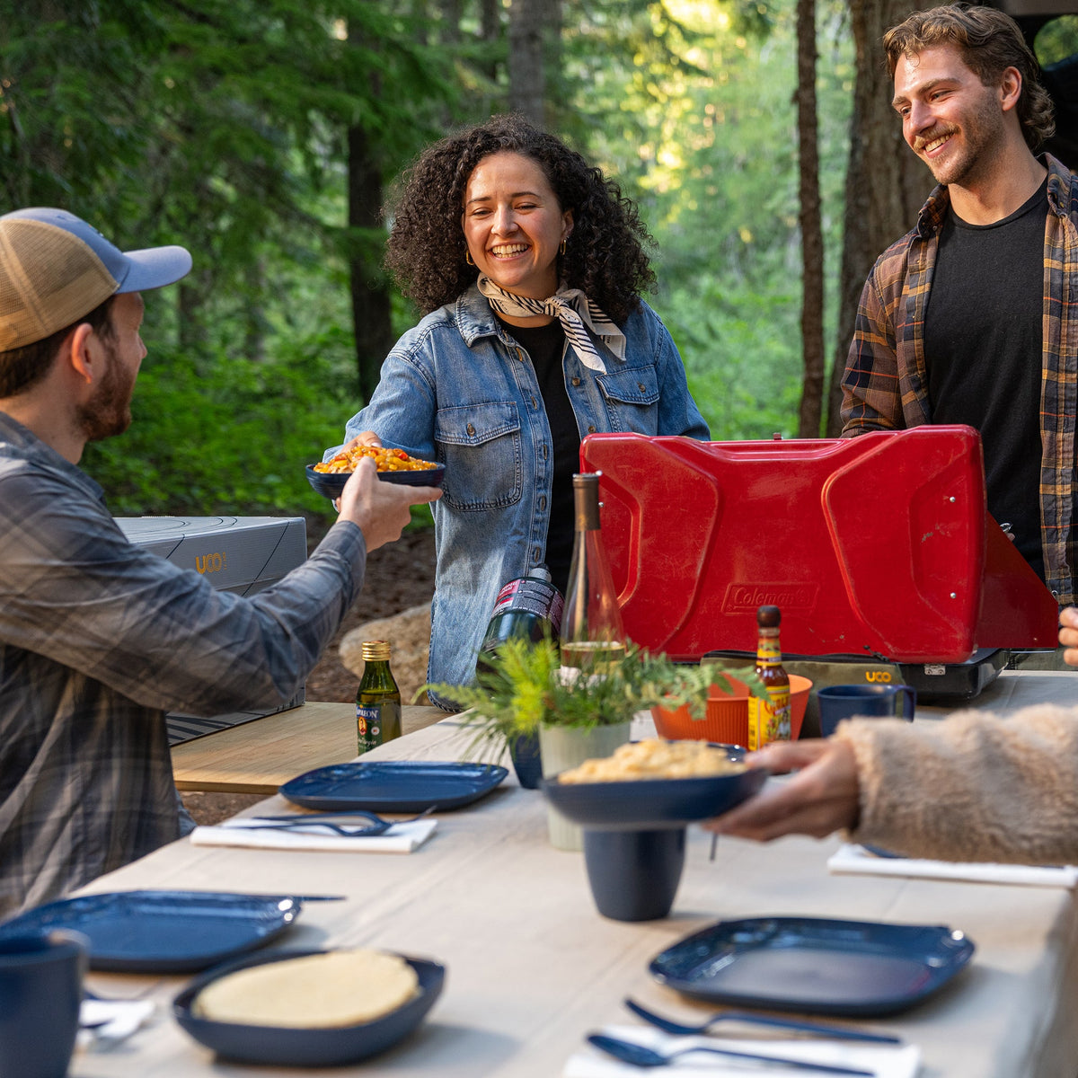 People at an outdoor picnic table using the UCO utensil set while passing a red cooler
