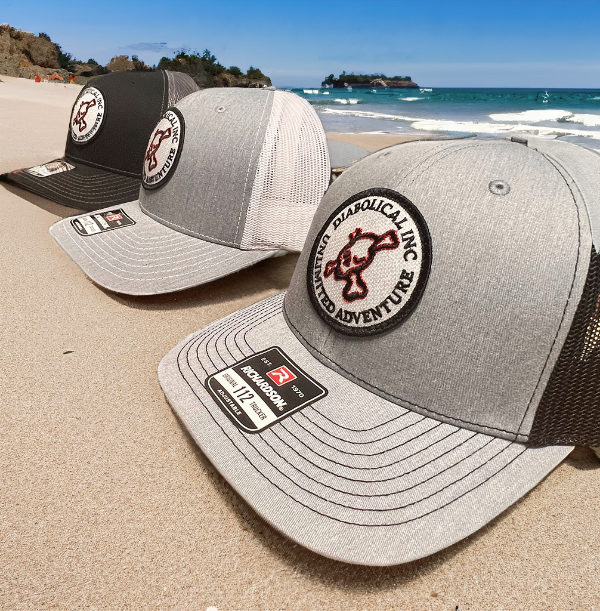 Both Diabolical Inc trucker hat colorways on a sandy beach