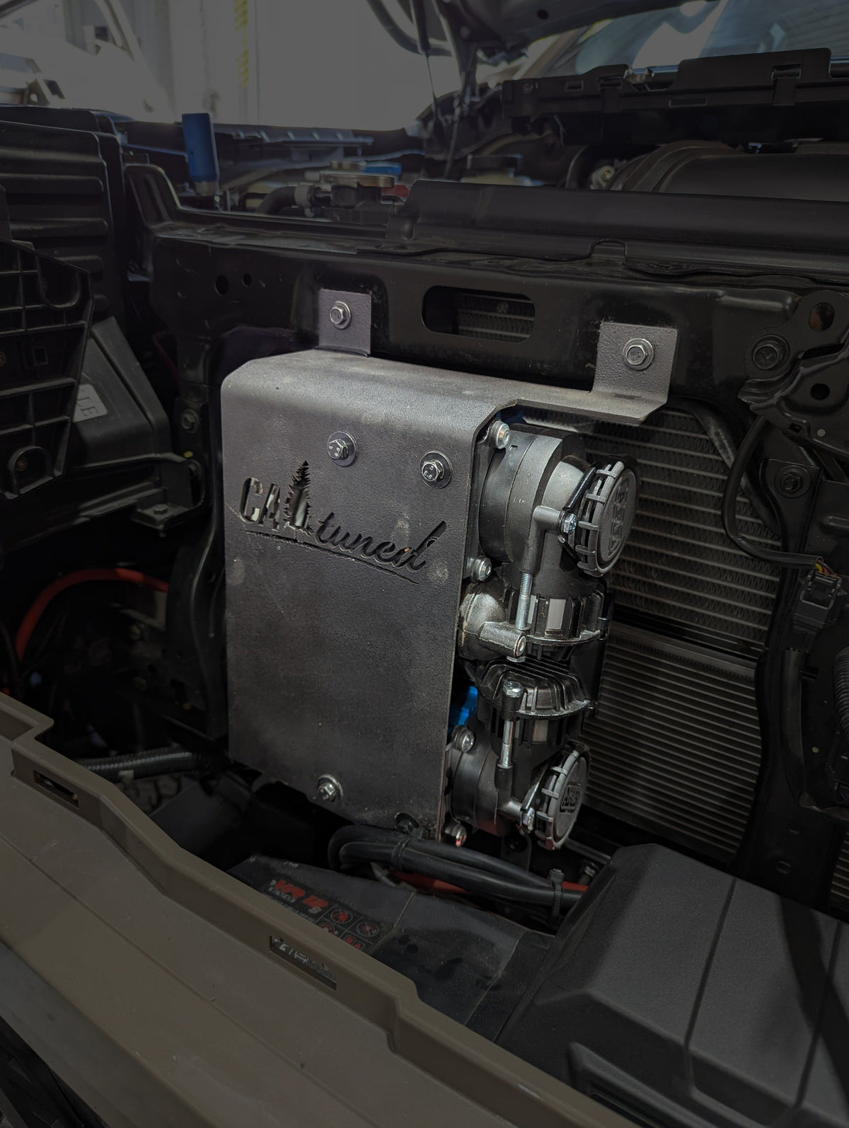 Silver air compressor on the mount in an engine bay, side view
