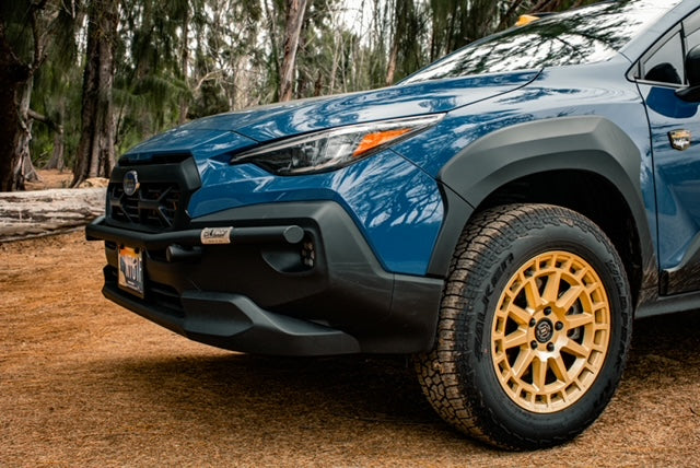 Close view of a black brush bar on the front of a blue Subaru SUV with a gold wheel