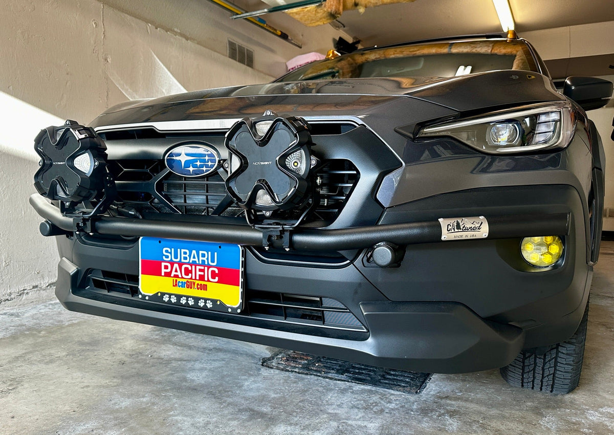 Subaru SUV with a brush bar and two black light pods parked in a garage