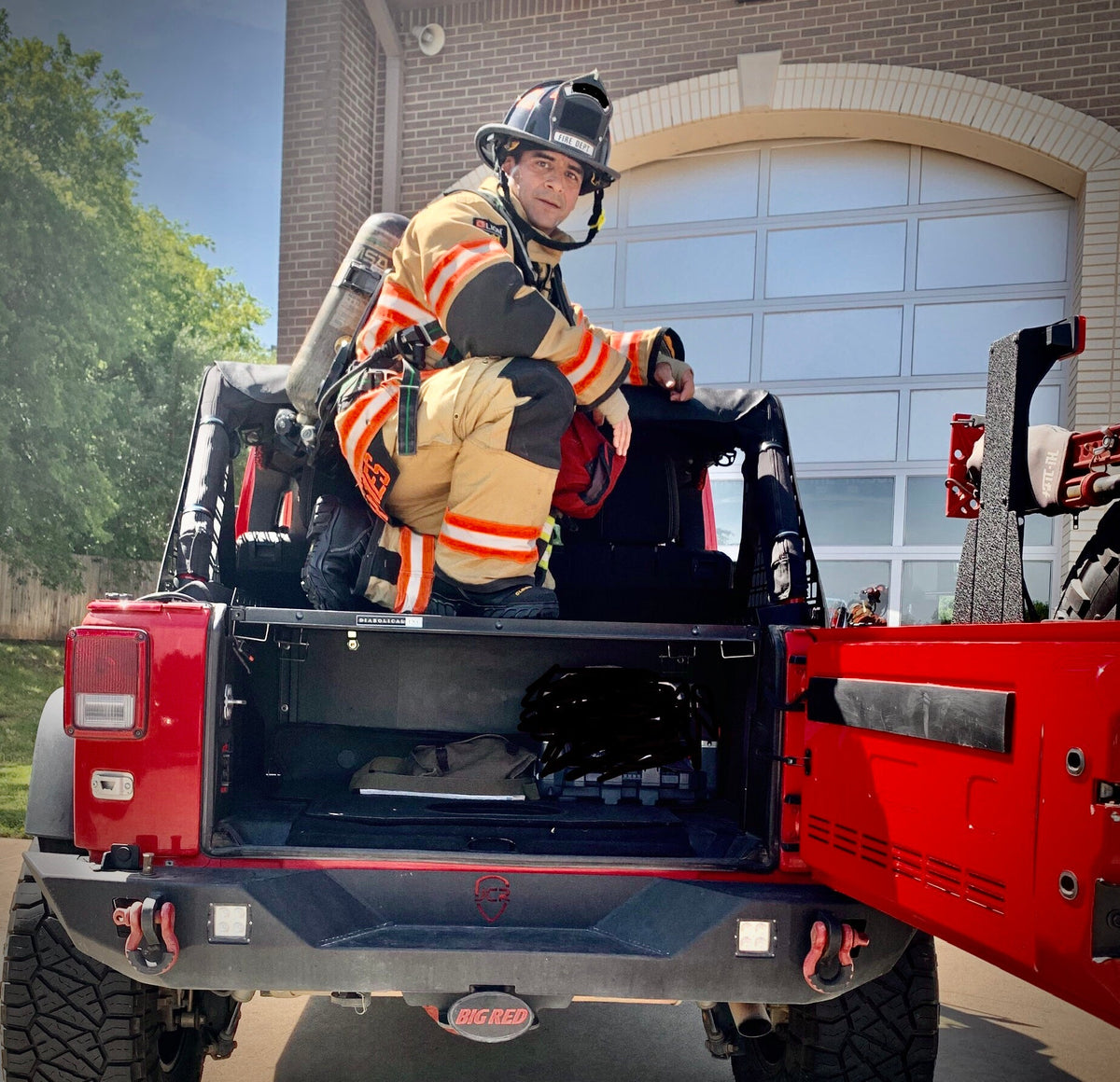 Firefighter in turnout gear sitting on top of a Slipstream enclosure with the tailgate open