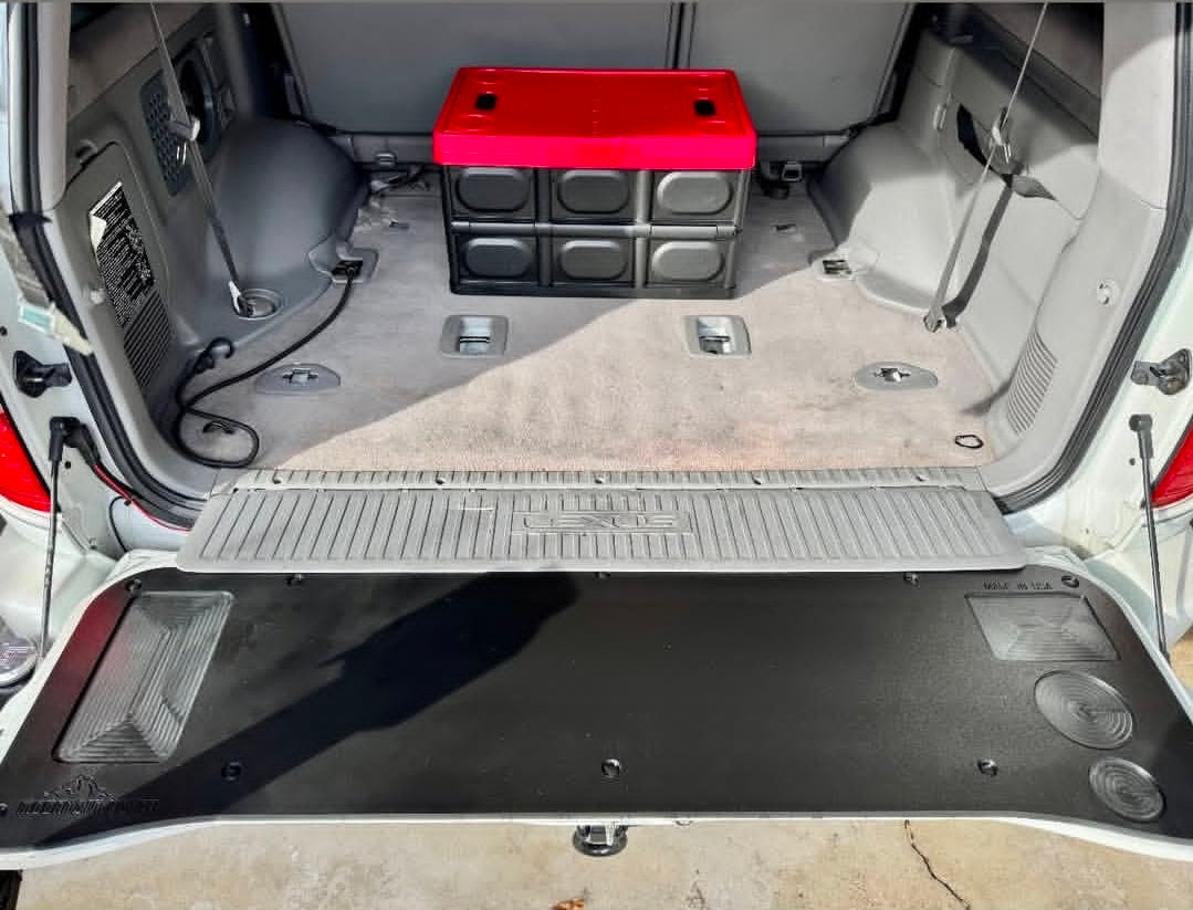 Rear view of a 100 Series Land Cruiser with the Mountain Hatch panel installed on the lowered tailgate, cargo area with storage crates behind