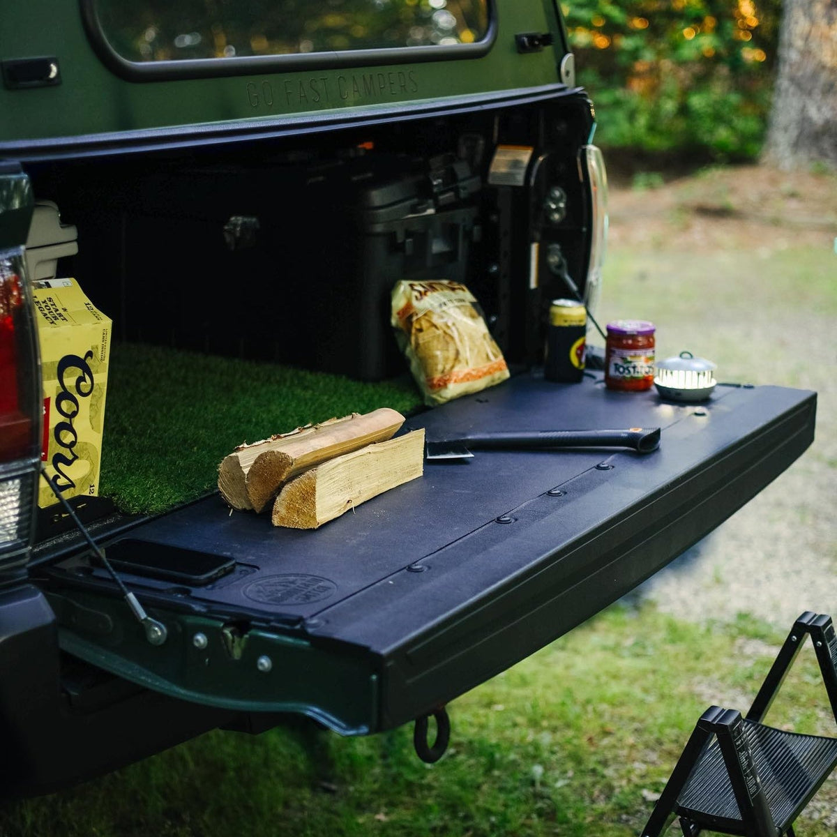 Mountain Hatch tailgate table on a green Toyota Tacoma tailgate at camp with firewood and camp kitchen gear