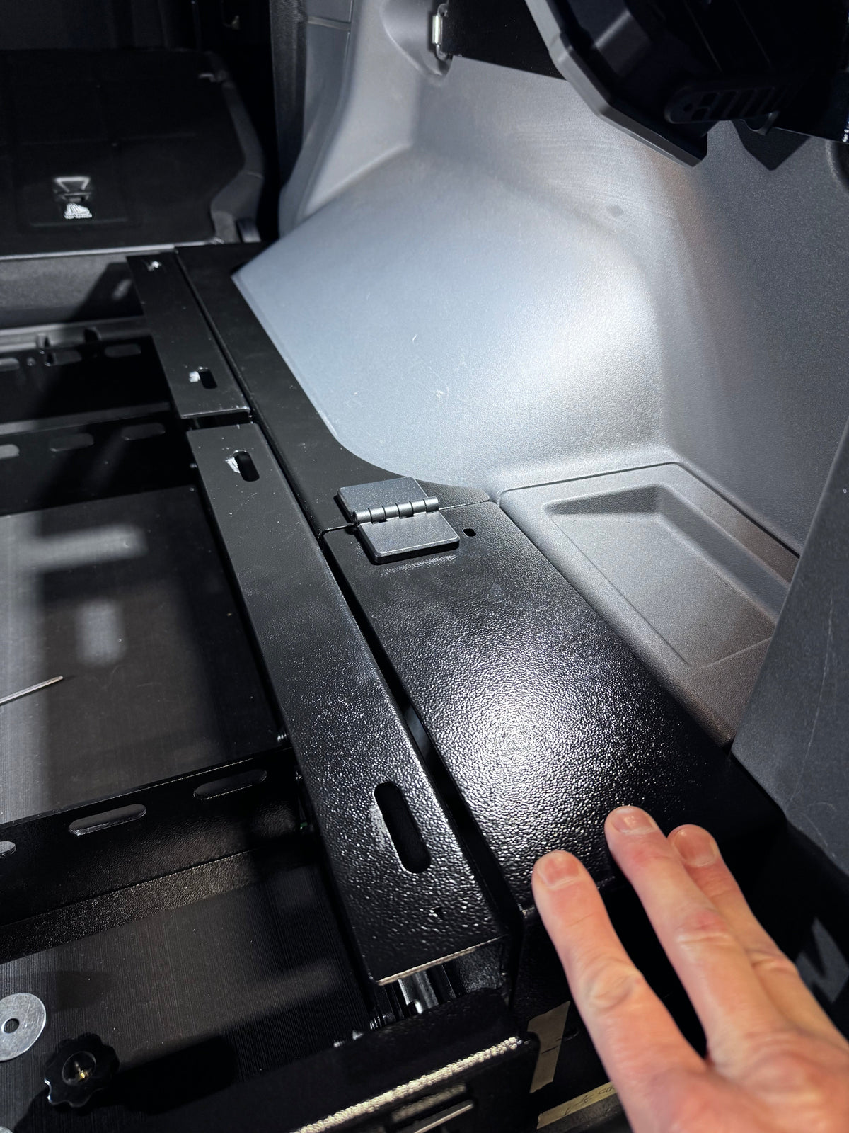 Hand pointing to the leveling panel bracket in the Grenadier cargo area