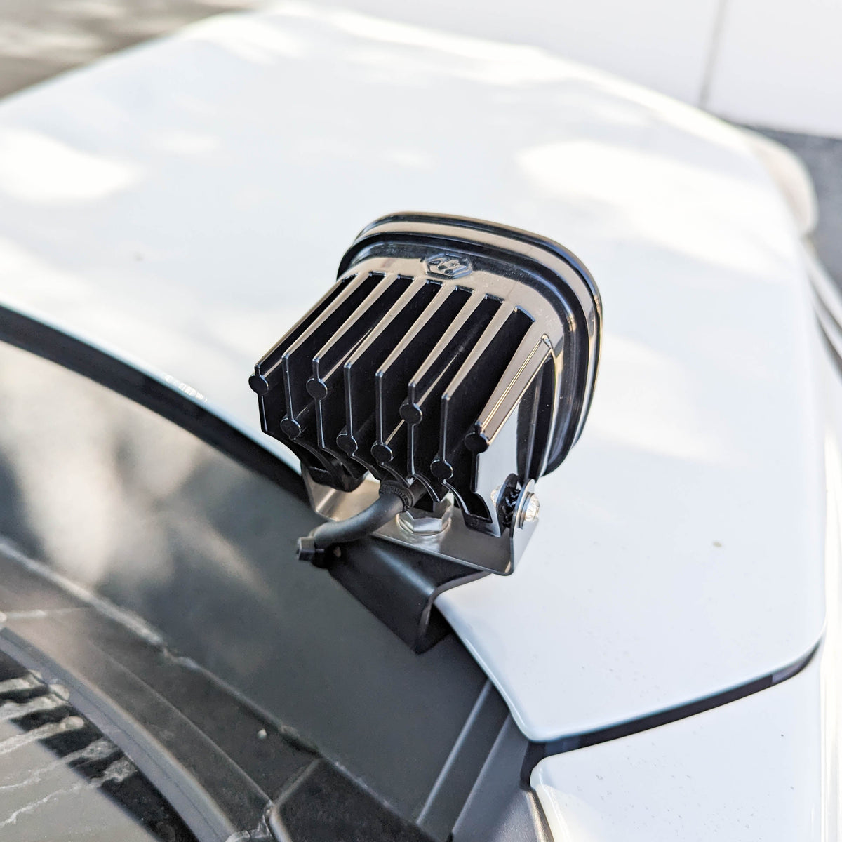 Black LED light pod on a bracket on a white hood